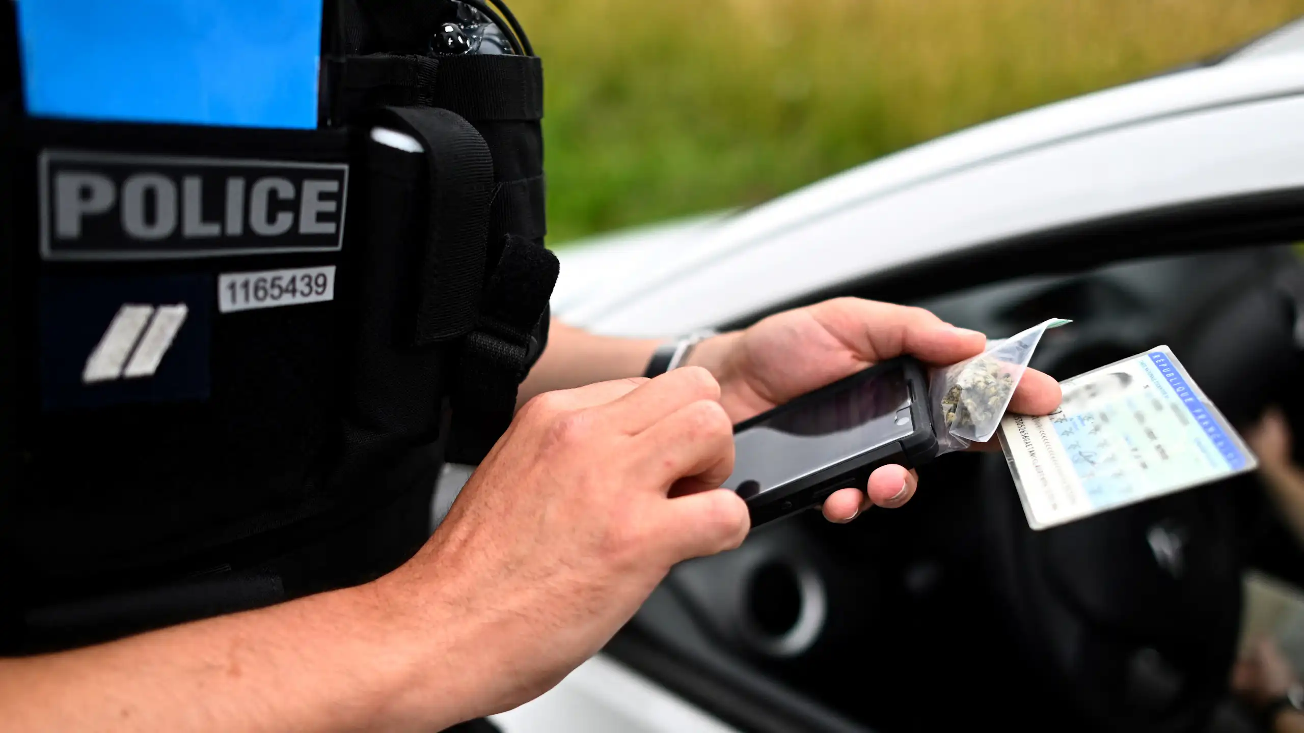 L’agent de police tient un sachet de cannabis et une carte d'identité en main et remplit un formulaire électronique d'amende forfaitaire sur un mobile.