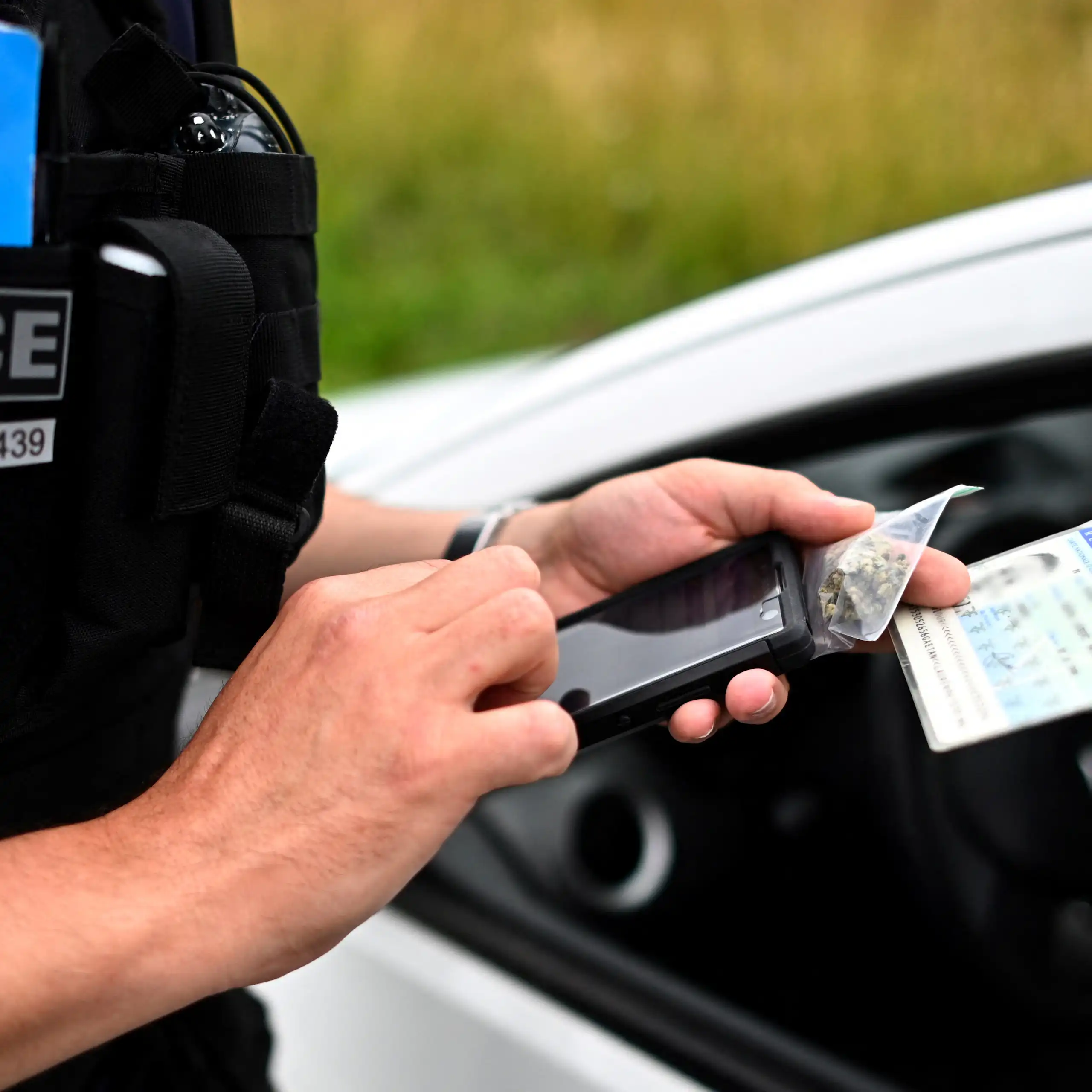 L’agent de police tient un sachet de cannabis et une carte d'identité en main et remplit un formulaire électronique d'amende forfaitaire sur un mobile.