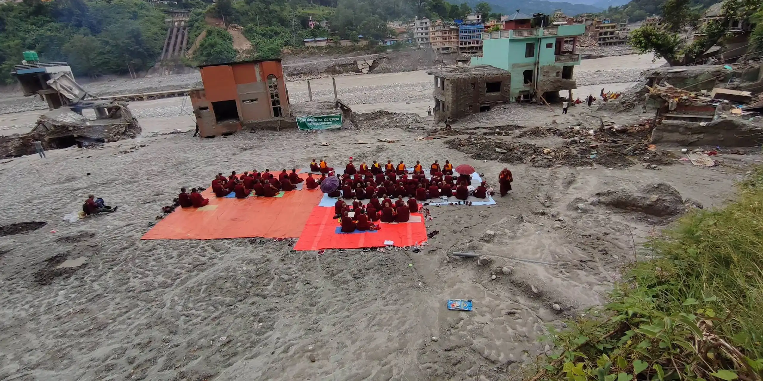 Buddhist monks sit on red tarps in a muddy expanse conducting death rituals
