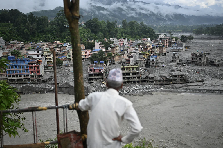 A man looks at the remains in the aftermath of flash floods. Cement structures that were once multi-story homes and businesses are covered in mud.