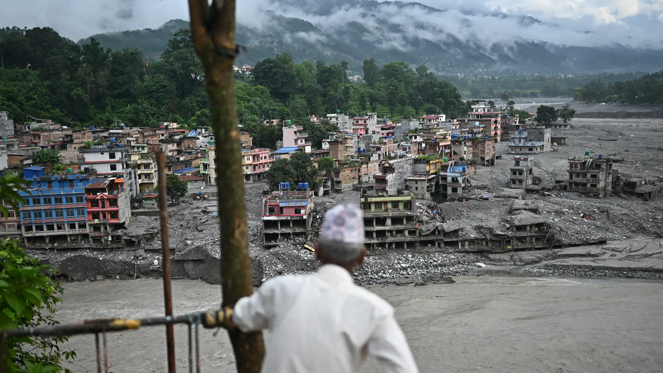 A man looks at the remains in the aftermath of flash floods. Cement structures that were once multi-story homes and businesses are covered in mud.