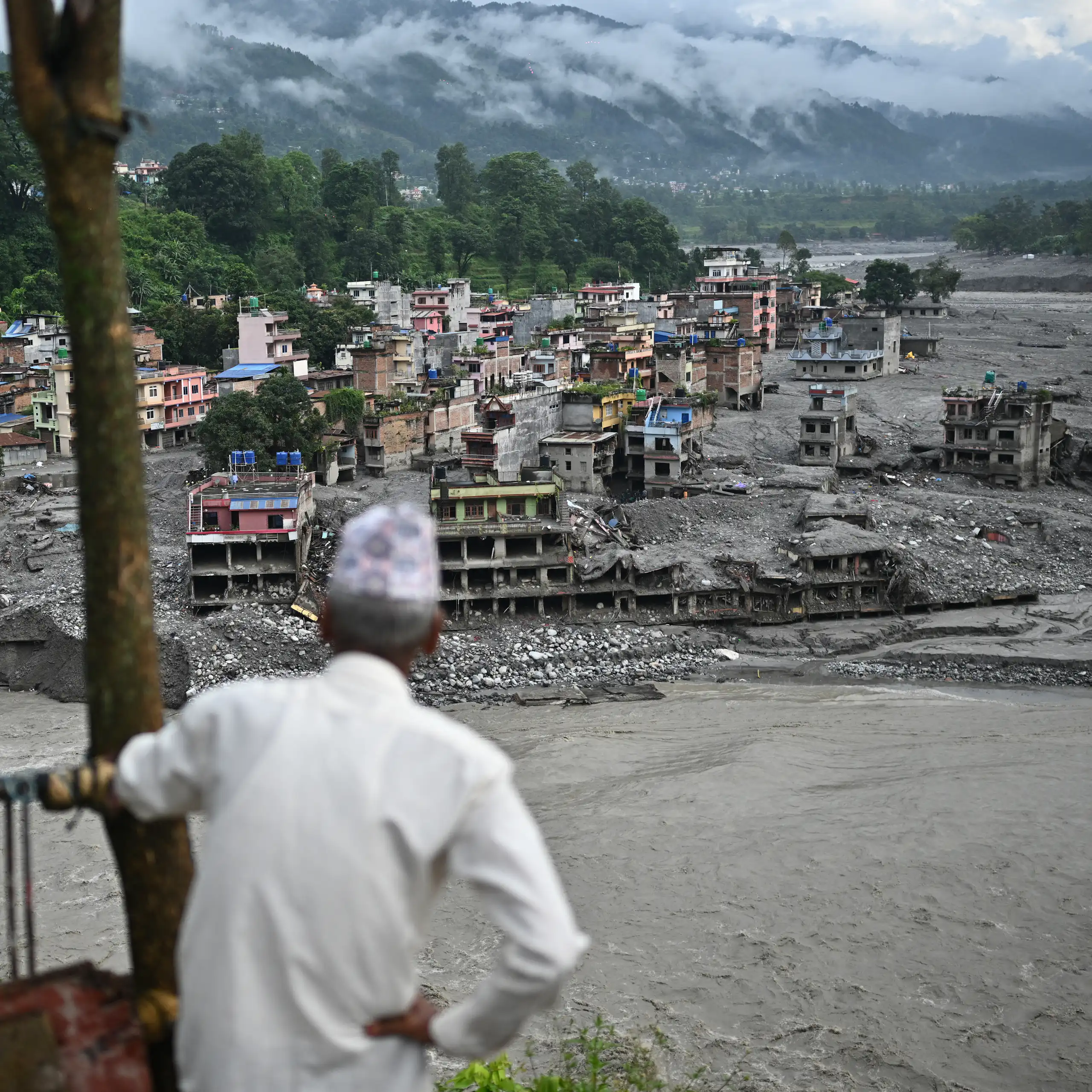 A man looks at the remains in the aftermath of flash floods. Cement structures that were once multi-story homes and businesses are covered in mud.