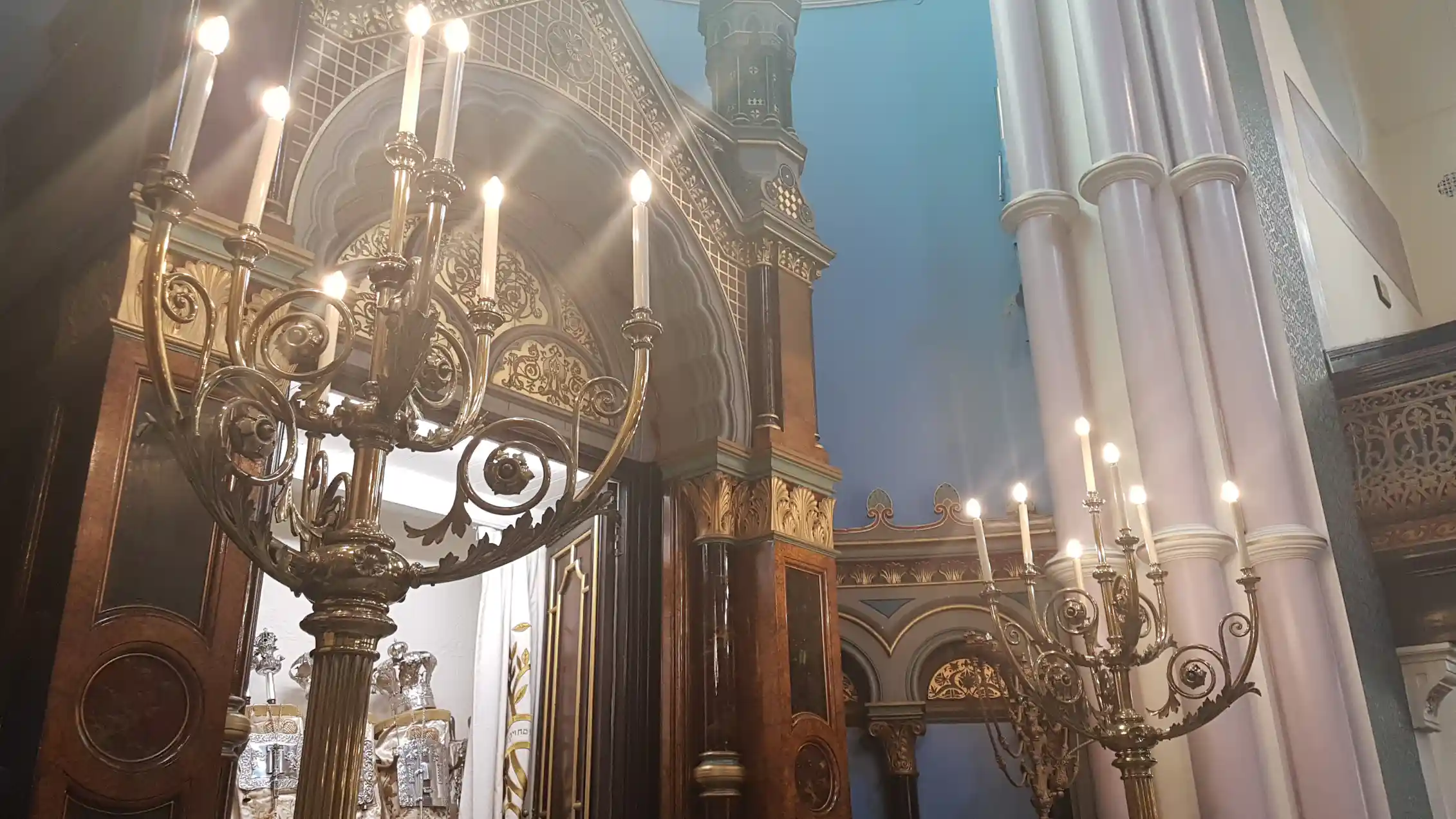 A large cabinet-like structure stands open, containing scrolls encased in silver holders.