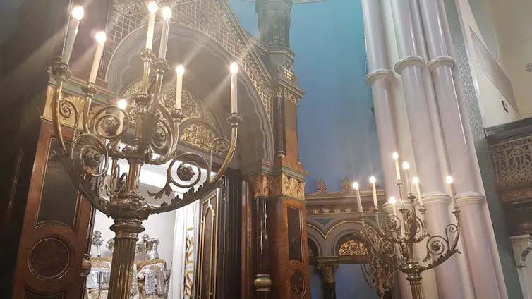 A large cabinet-like structure stands open, containing scrolls encased in silver holders.