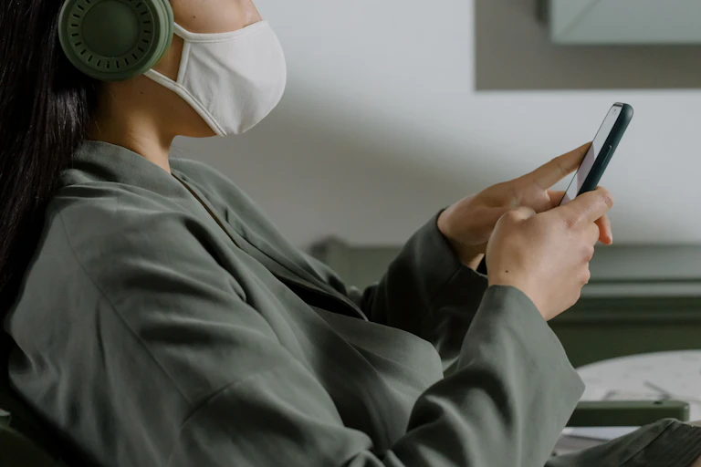 Person wearing a mask over their mouth and nose and looking at a phone