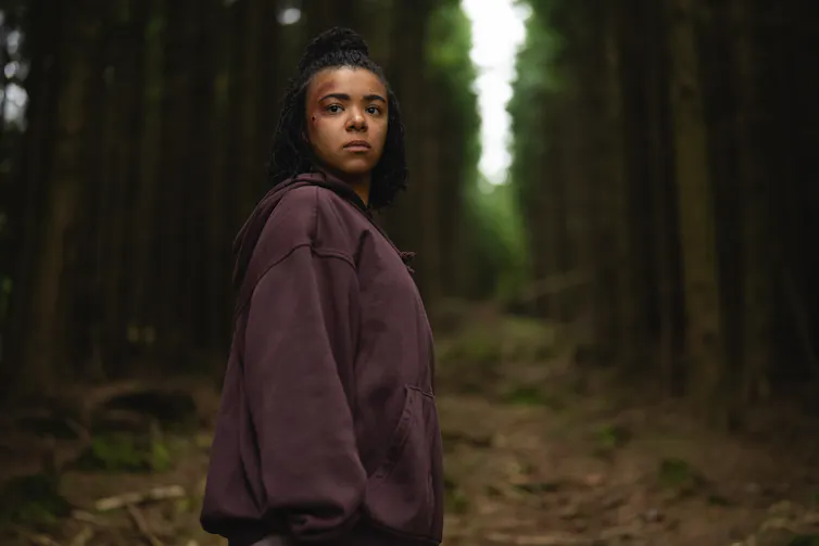 young woman in brown jumper standing in eerie dark woodland