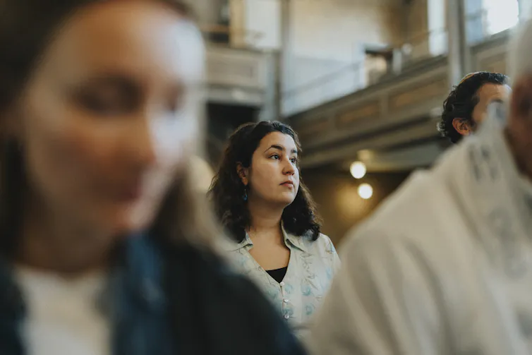 A woman stares into the distance as she stands amid other people in a sanctuary.