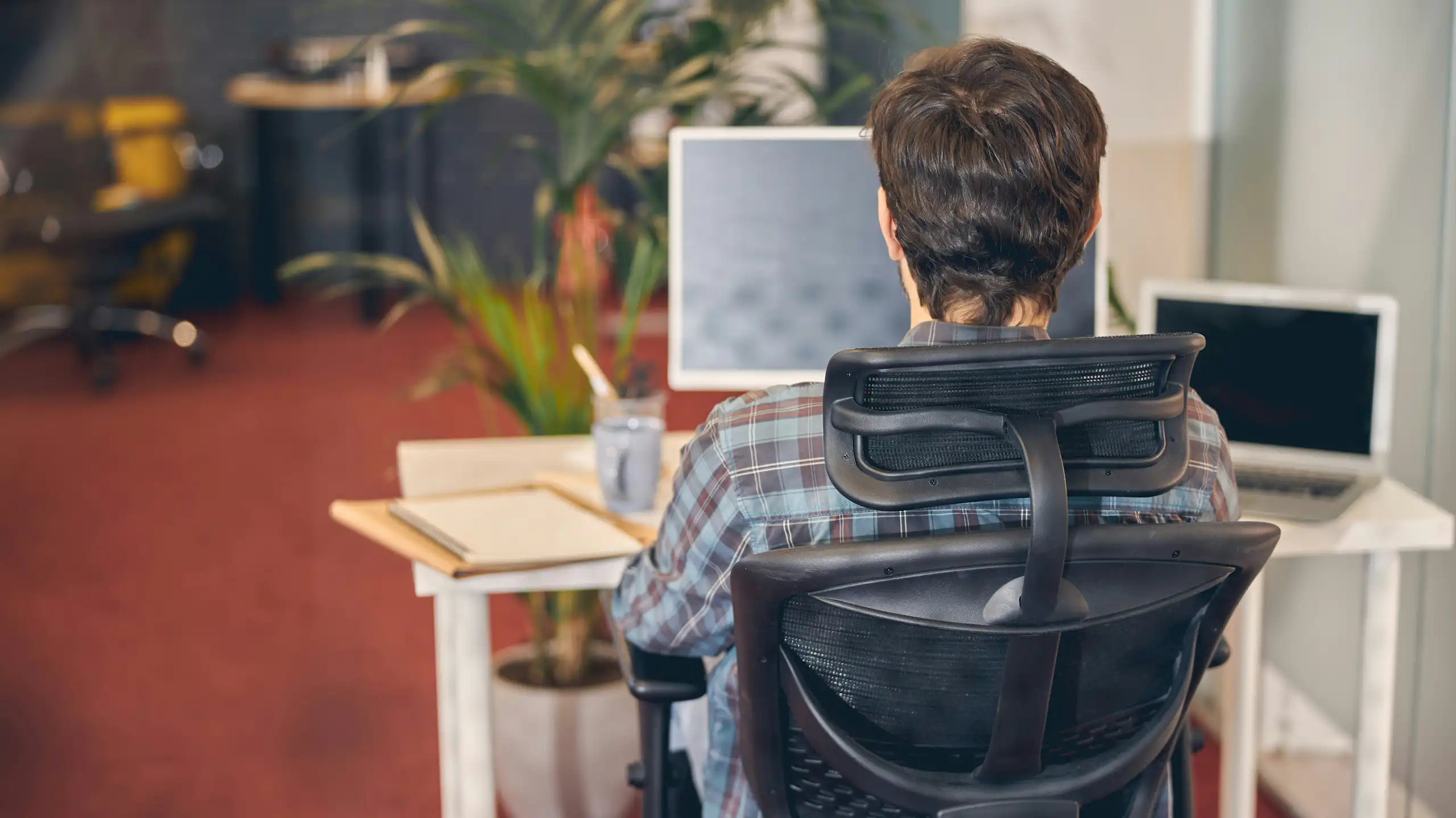 A person sitting in an ergonomic chair, facing away from the camera toward a computer screen