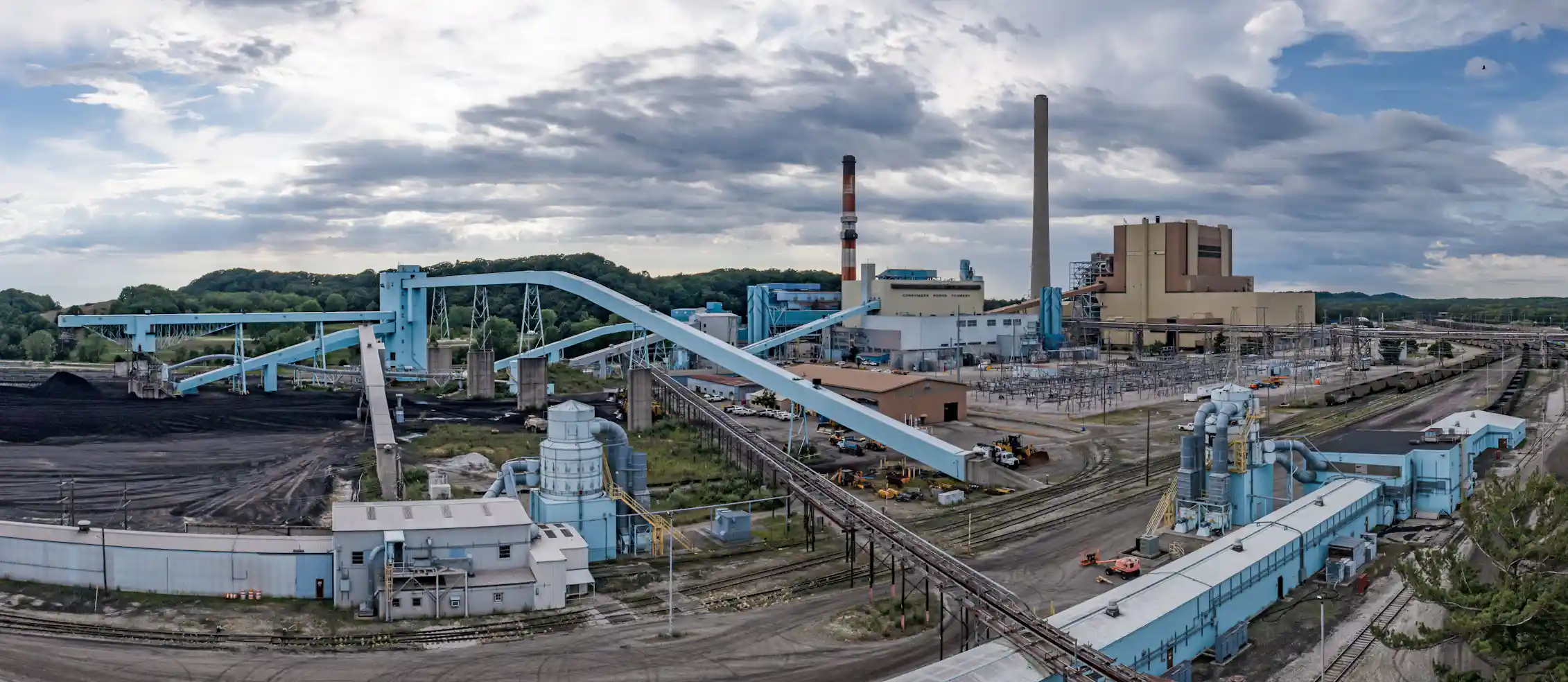 A large industrial facility includes piles of dark material and tall smokestacks.