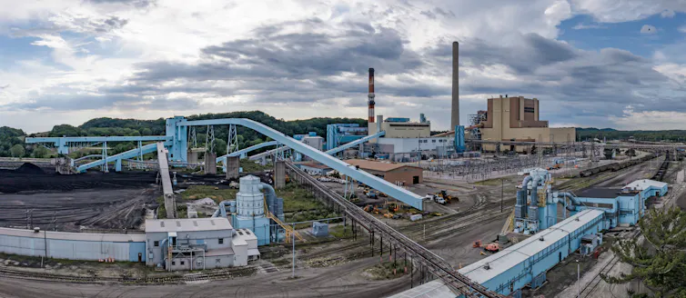 A large industrial facility includes piles of dark material and tall smokestacks.