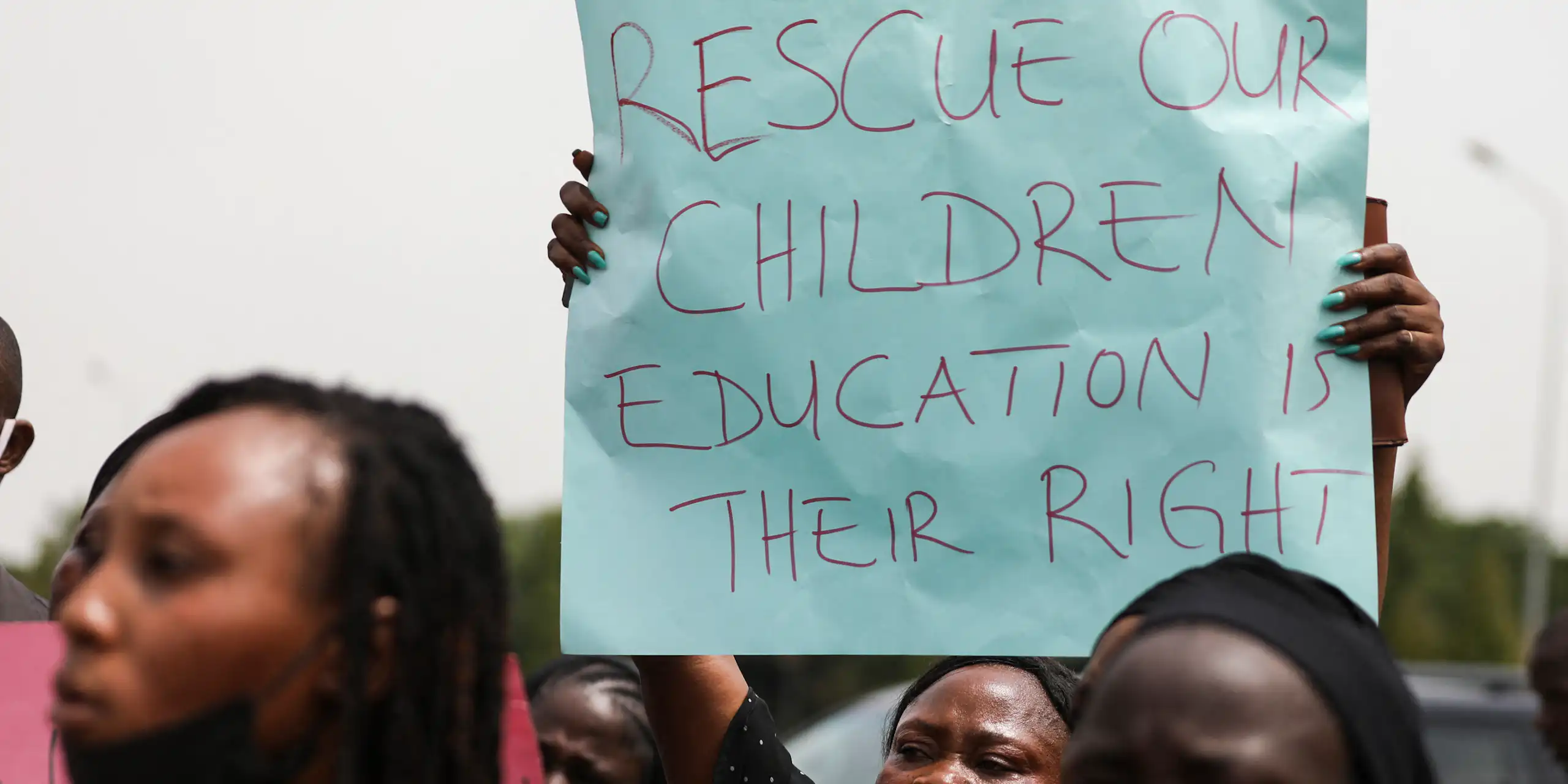 Woman holding a poster that says "rescue our children / education is their right"