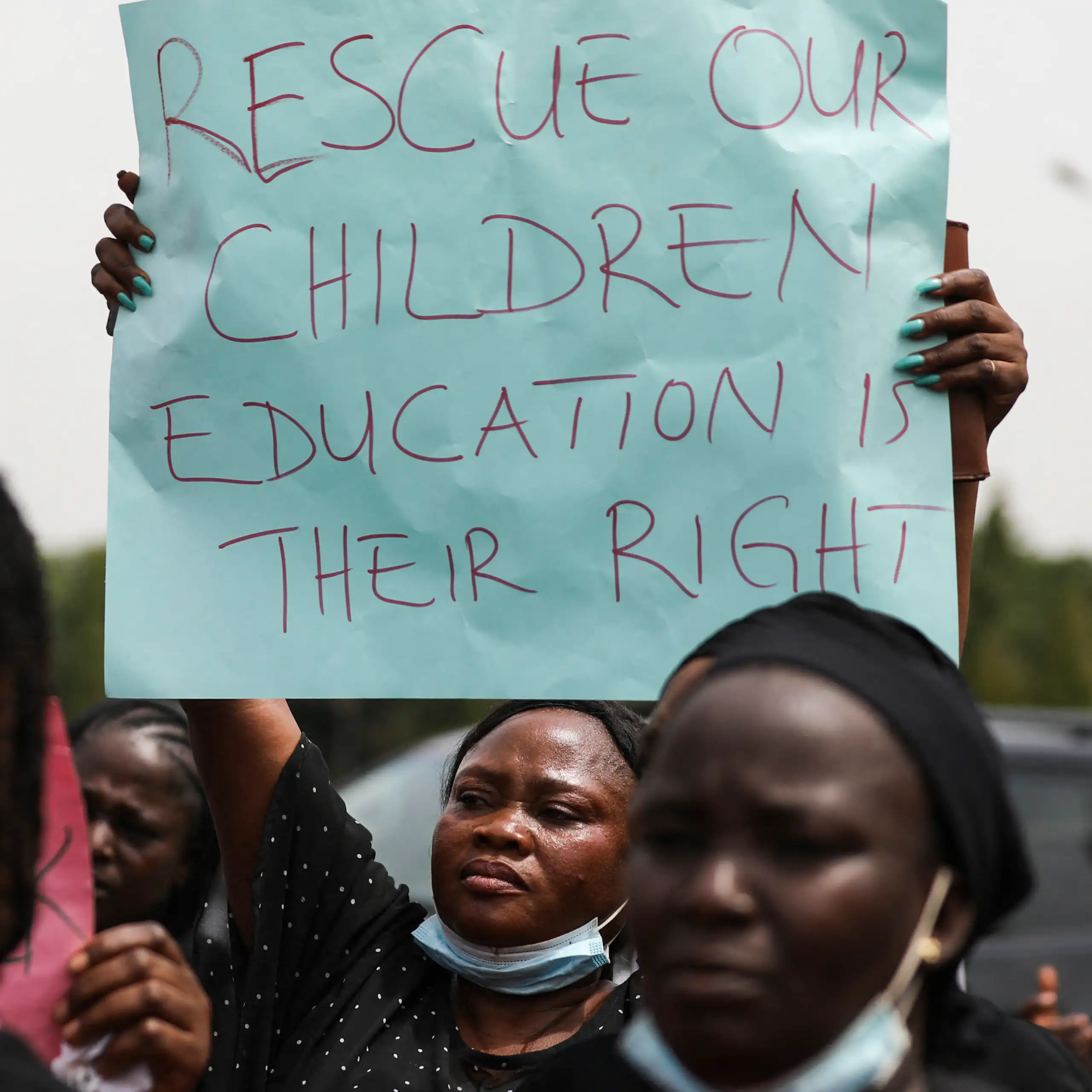 Woman holding a poster that says "rescue our children / education is their right"