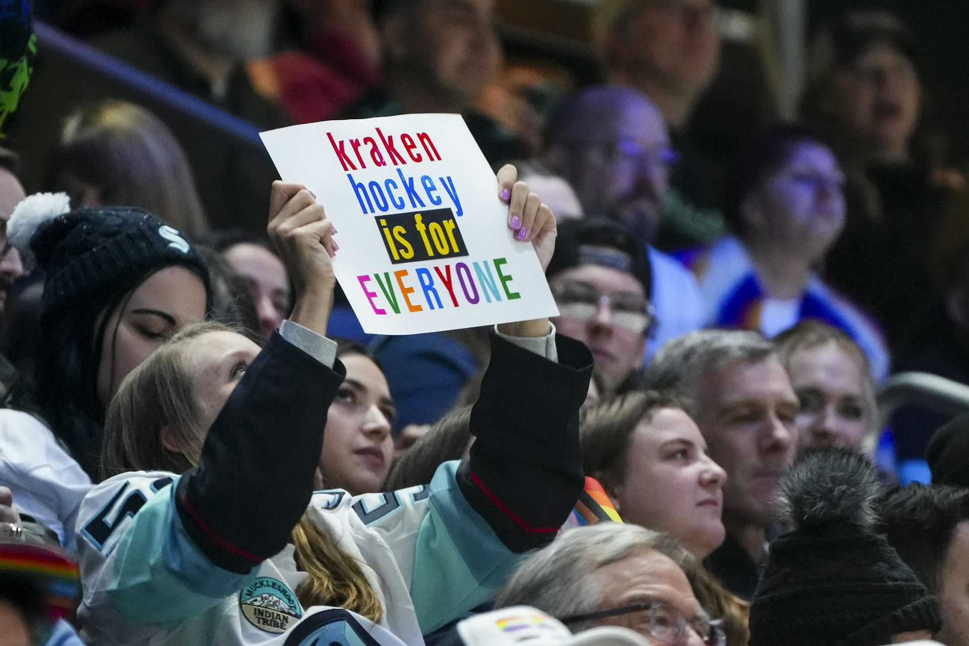 A spectator at a hockey game holds a sign up while wearing a hockey jersey