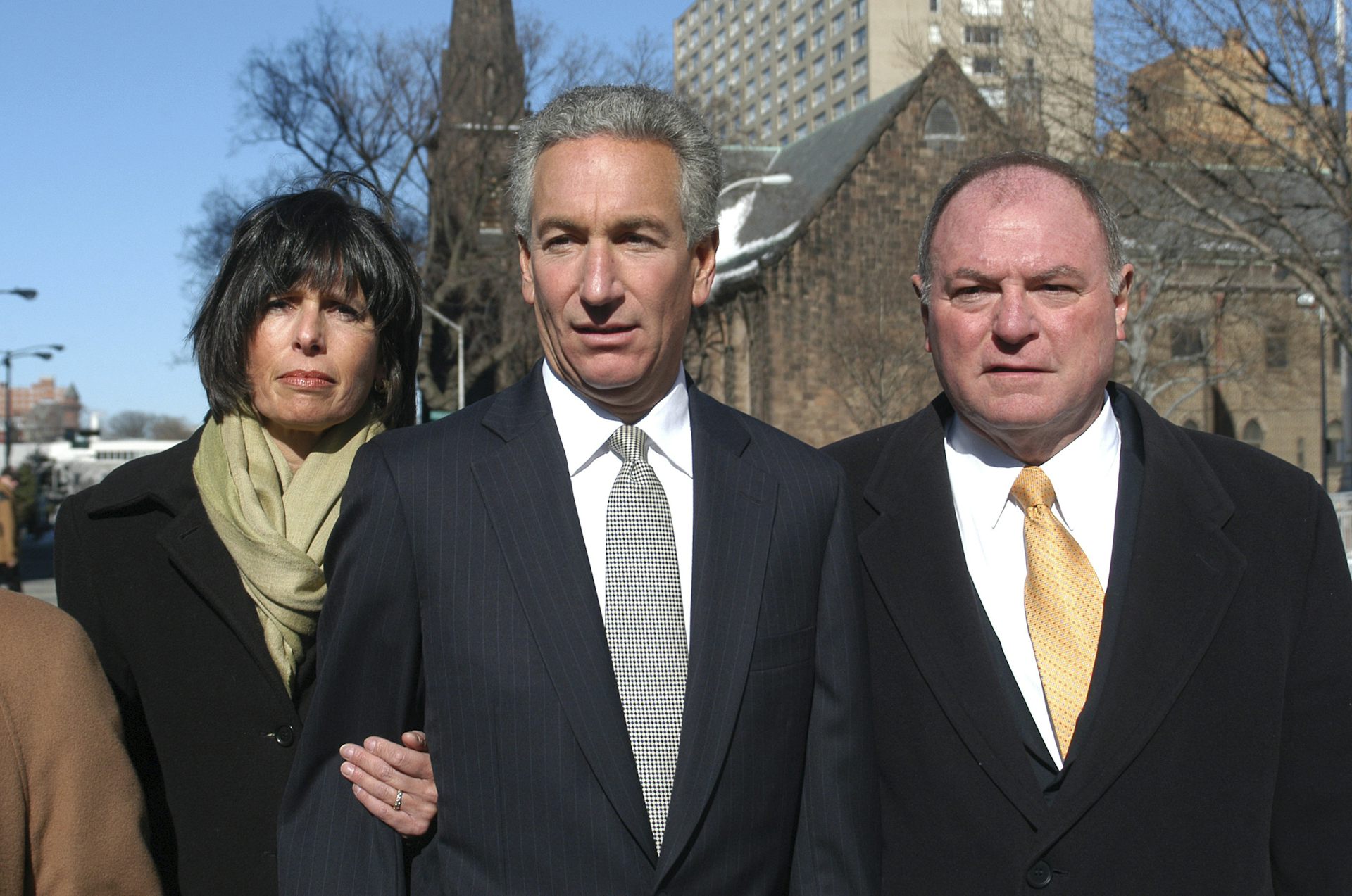 A man stands outside a courthouse with his wife and his attorney.