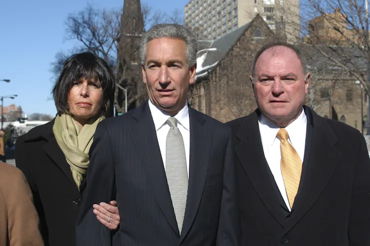 A man stands outside a courthouse with his wife and his attorney.