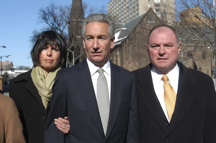 A man stands outside a courthouse with his wife and his attorney.
