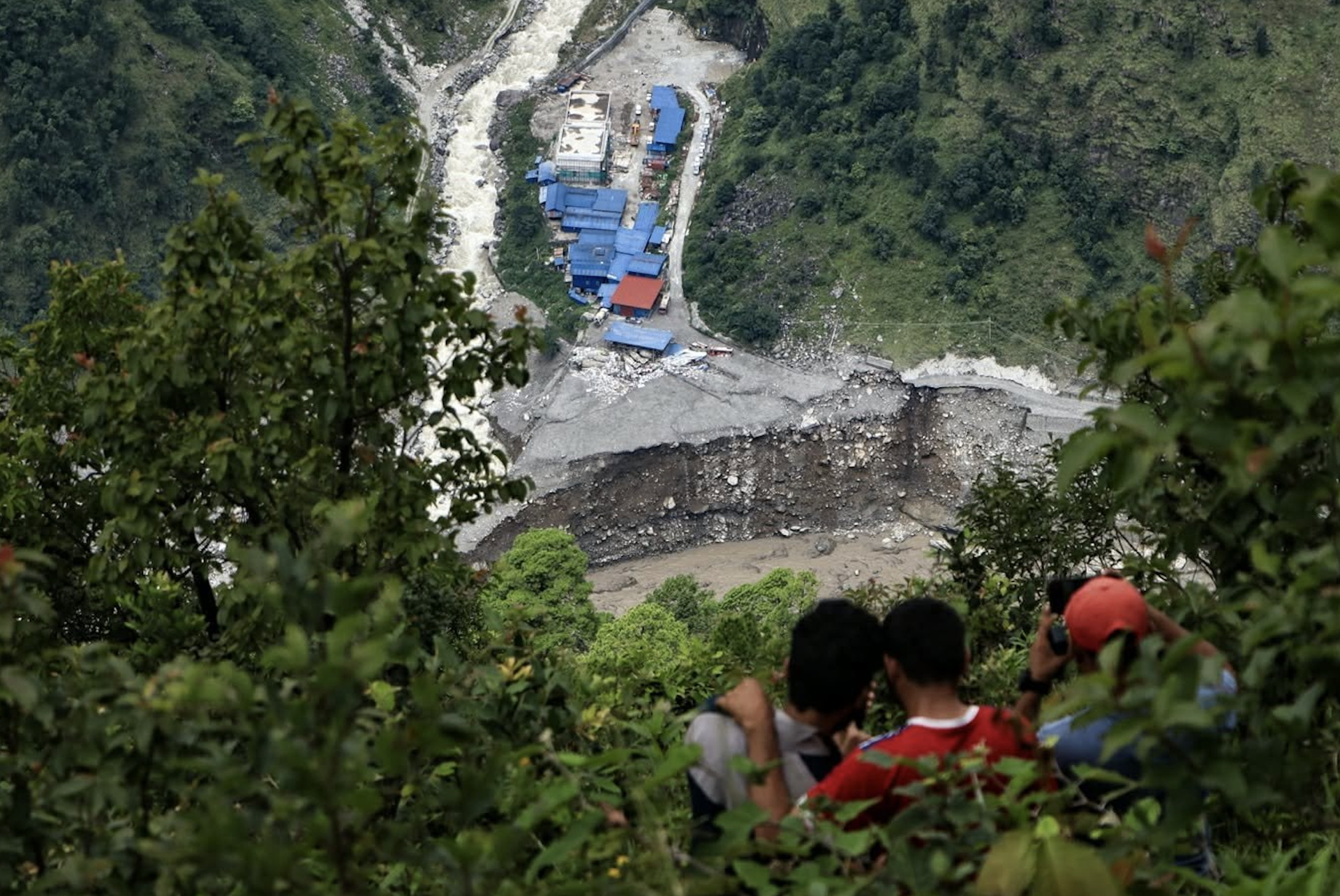 People stand on a hill looking down at a damaged hydropower plant.