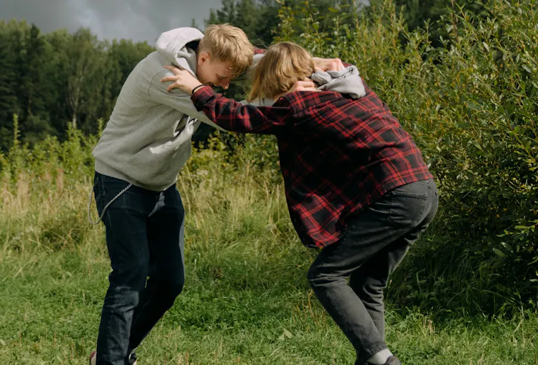 Teenage boys fighting and pushing each other in a field.