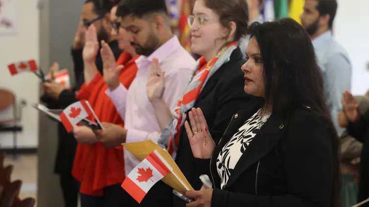 A row of people holding small Canadian flags as they swear an oath.