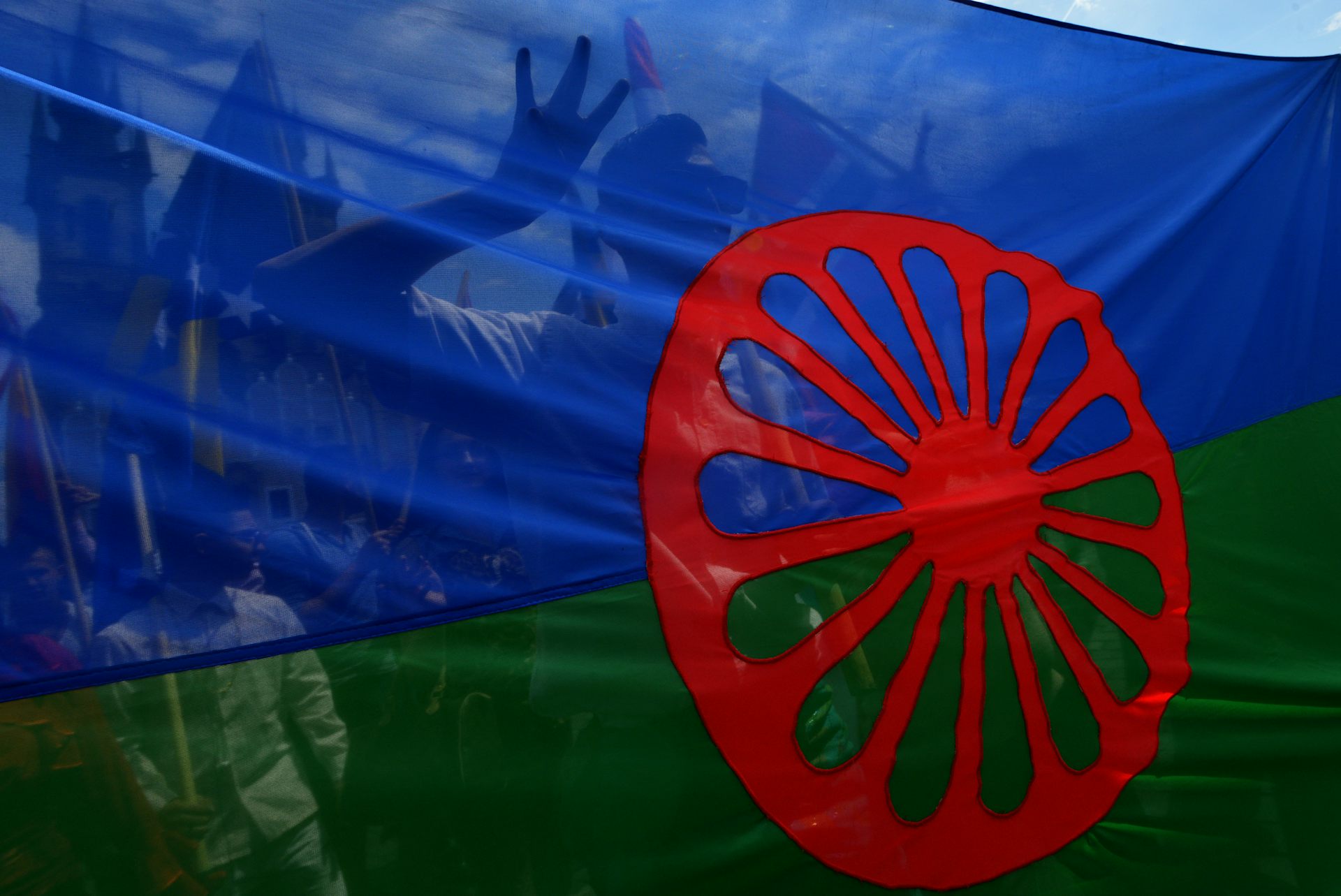 Gros plan sur le drapeau : une bande bleue et une bande verte horizontales surmontées d'une roue rouge de charriot placée au centre.