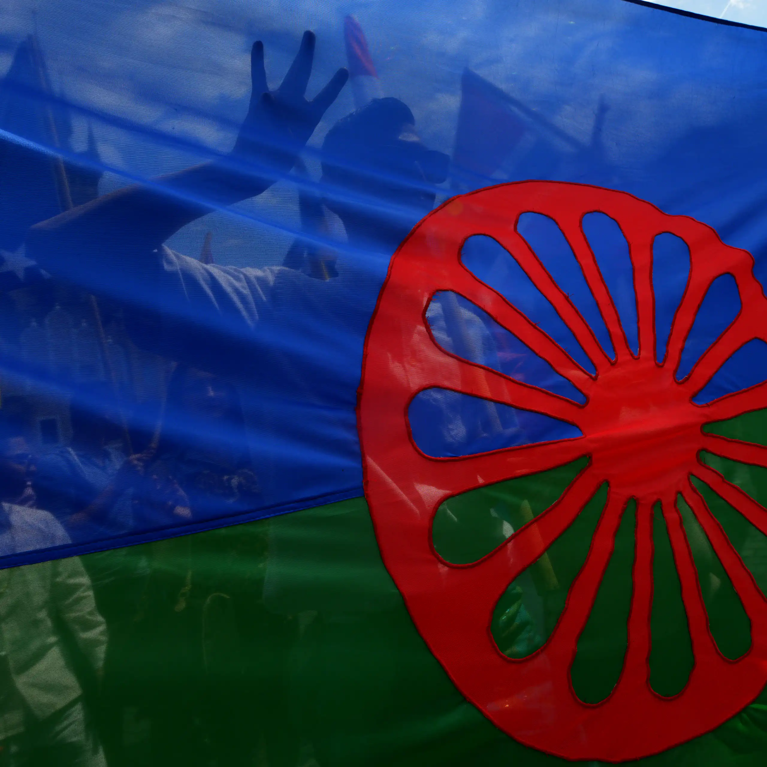 Gros plan sur le drapeau : une bande bleue et une bande verte horizontales surmontées d'une roue rouge de charriot placée au centre.