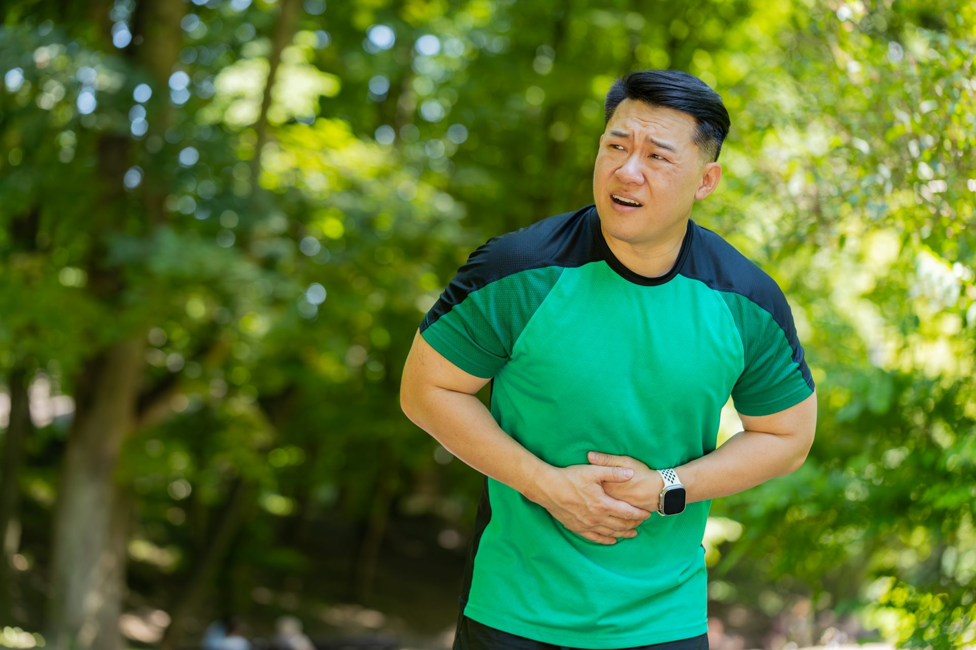 A man who is on a run holds onto his stomach while looking concerned.