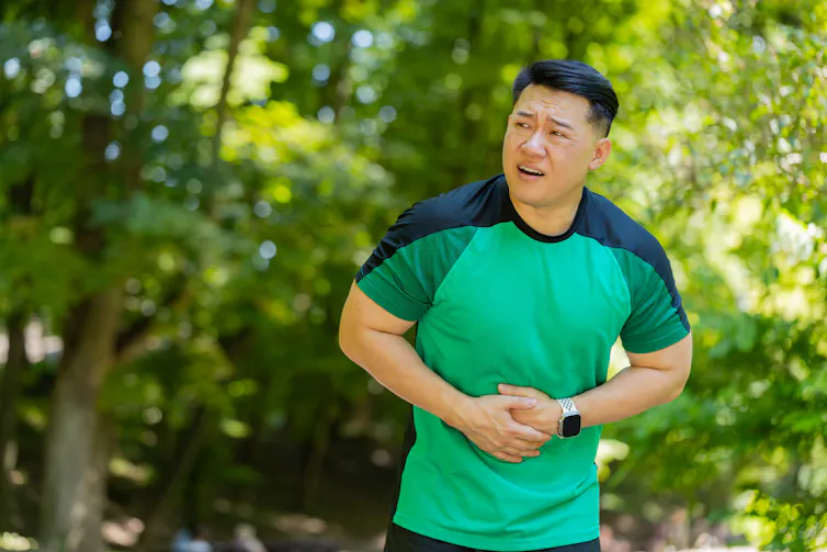 A man who is on a run holds onto his stomach while looking concerned.