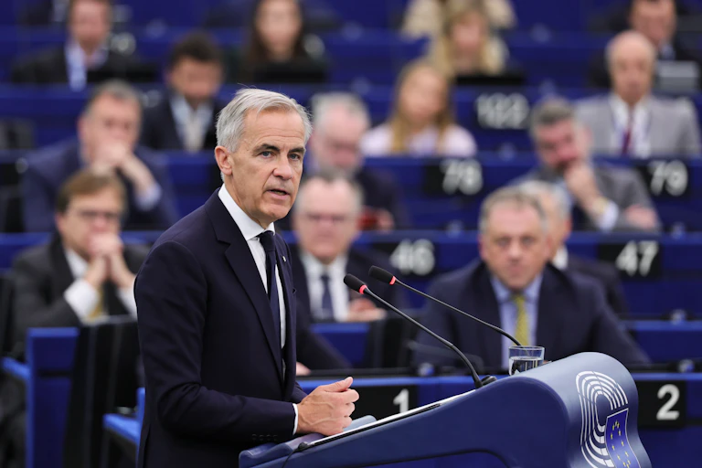 Canadian PM, Mark Carney, speaks at a podium with his audience in the background.
