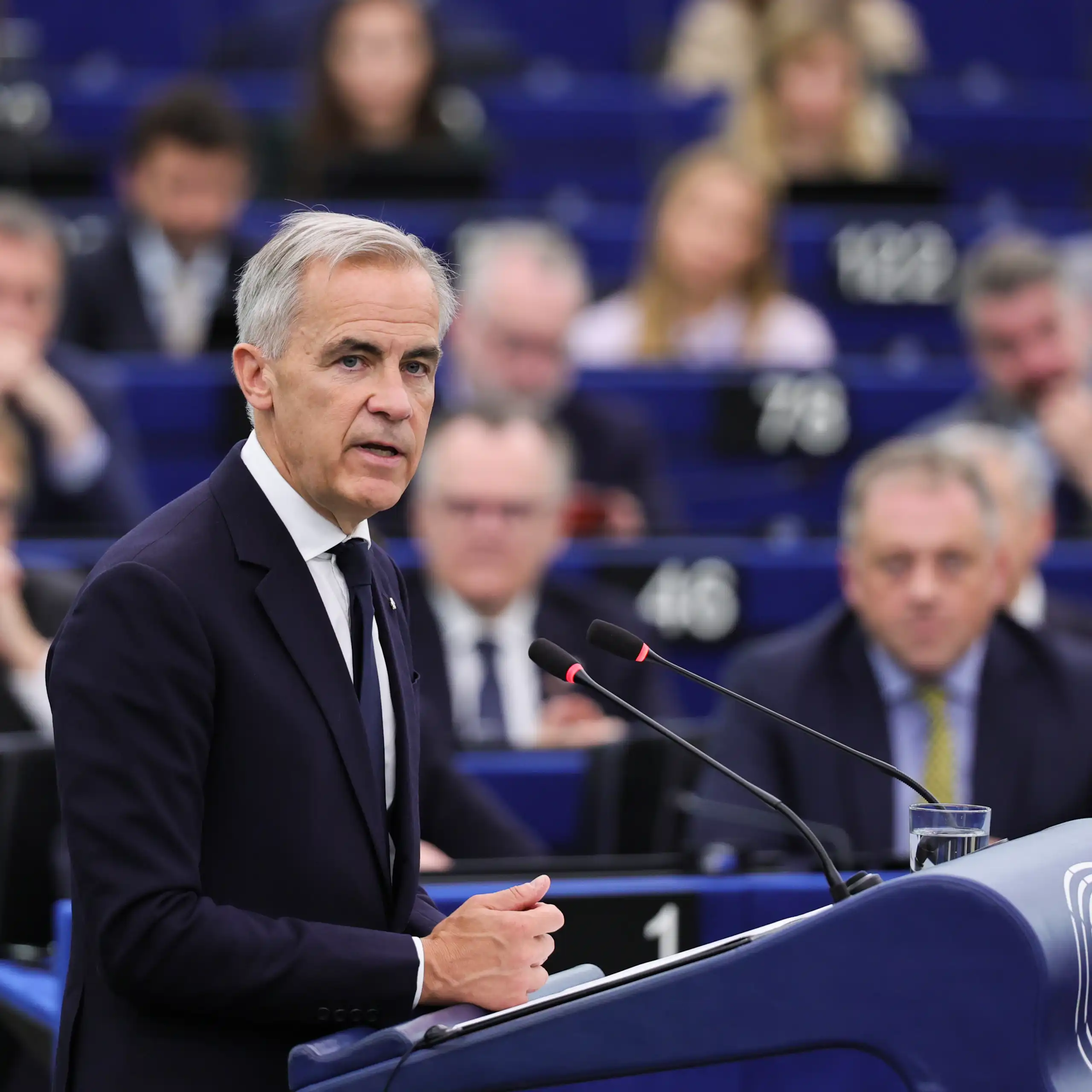 Canadian PM, Mark Carney, speaks at a podium with his audience in the background.