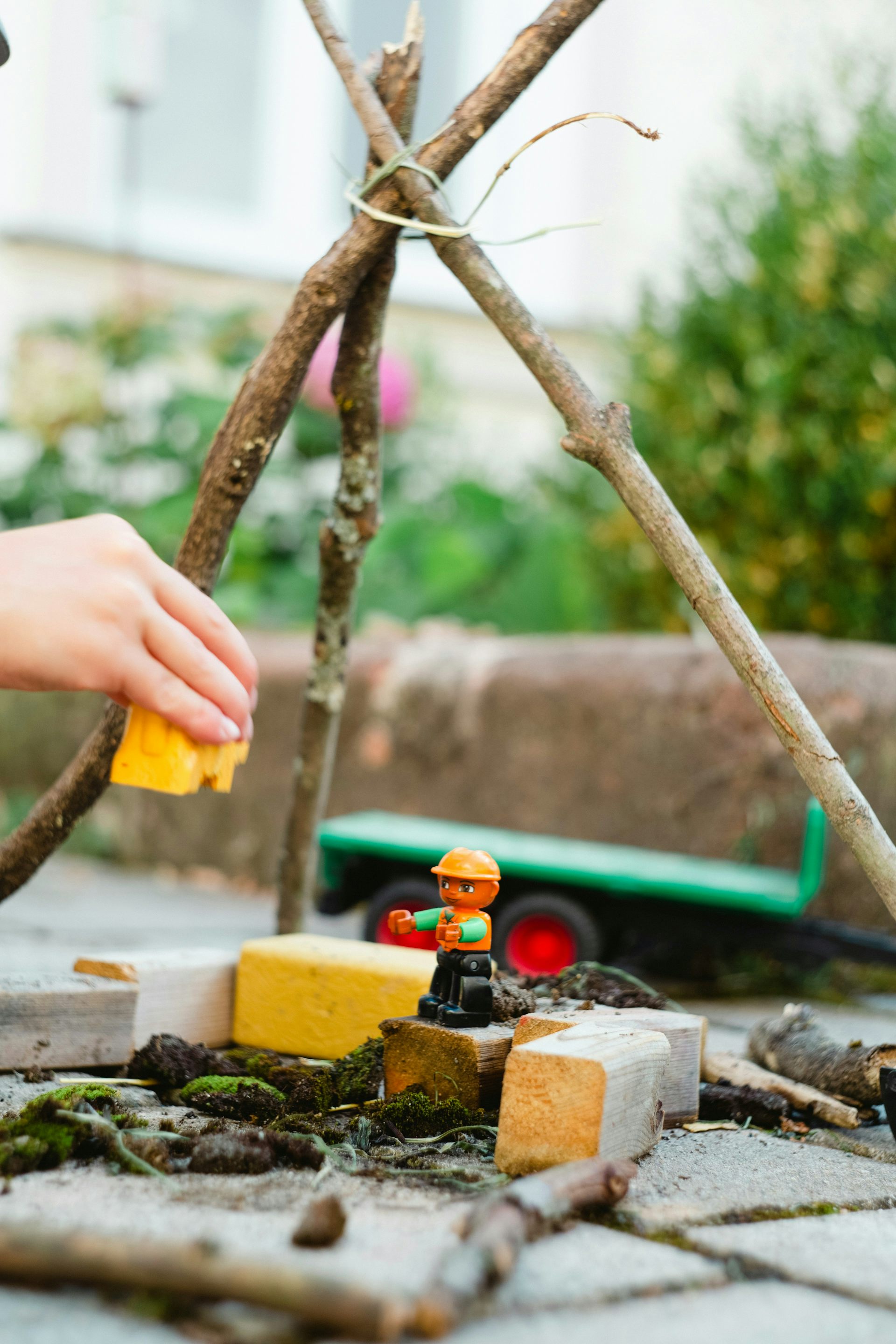 A child's hands playing with blocks and a stick structure outdoors.