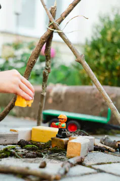 A child's hands playing with blocks and a stick structure outdoors.