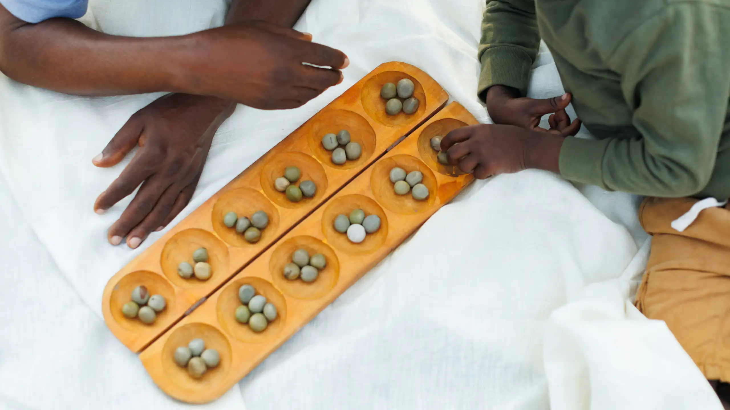 Adult and child hands seen atop a wooden game with the child's hands resting on round objects in a round hole.