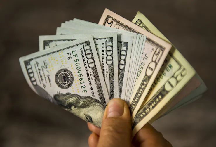 A person holds a big pile of U.S. cash between their fingers, including several $100 bills.