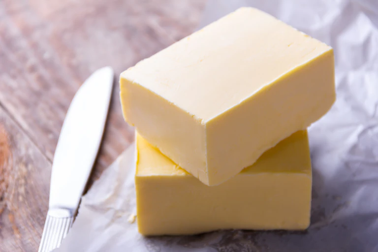 Two large blocks of butter stacked on top of a butter package with a silver knife on the left side.