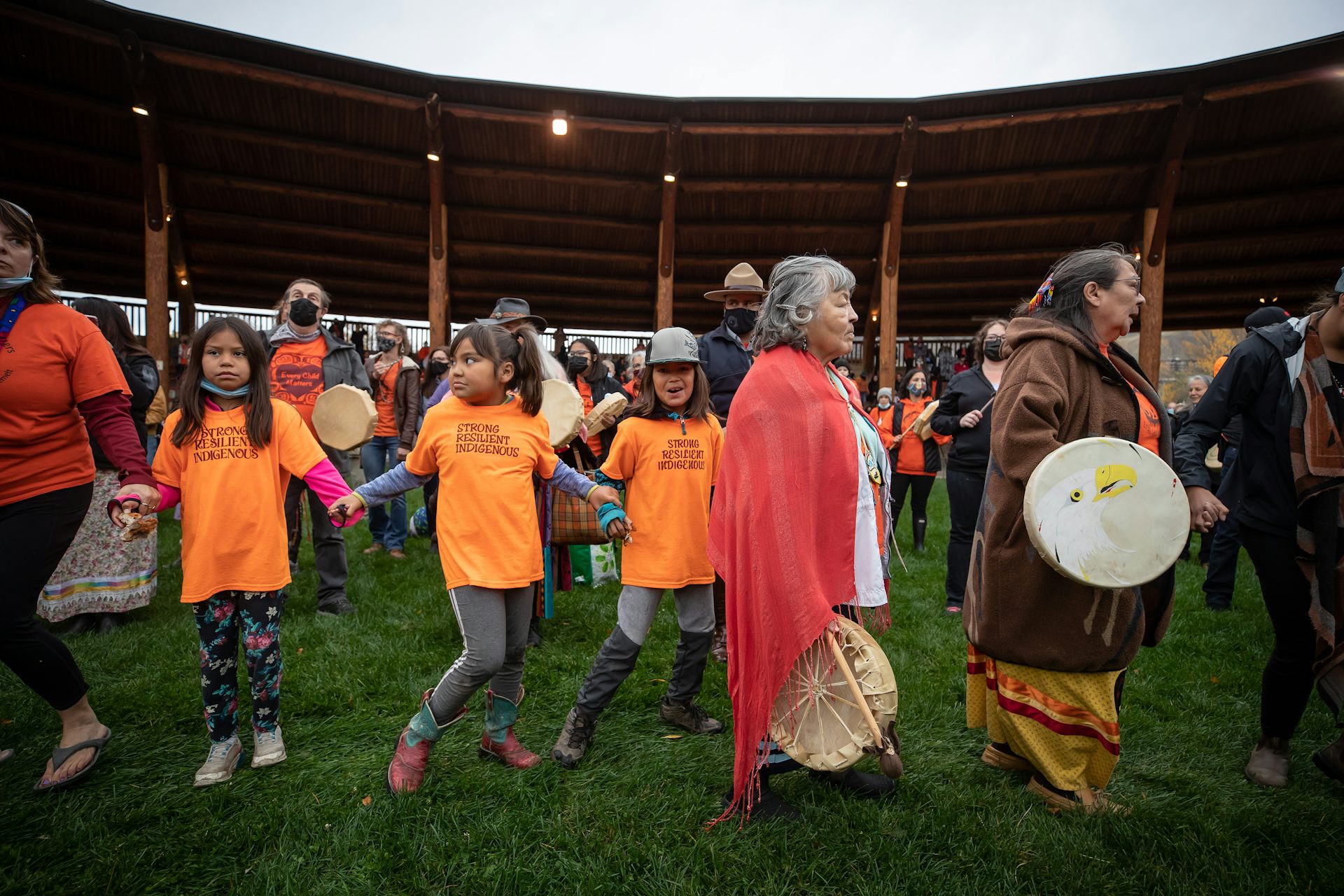 Young people in orange T-shirts dancing with people with drums in a circle.