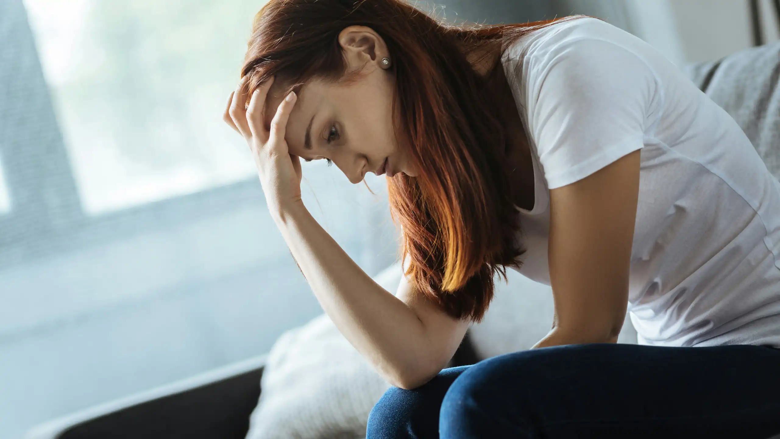 A young woman rests her head against her hand, looking distressed