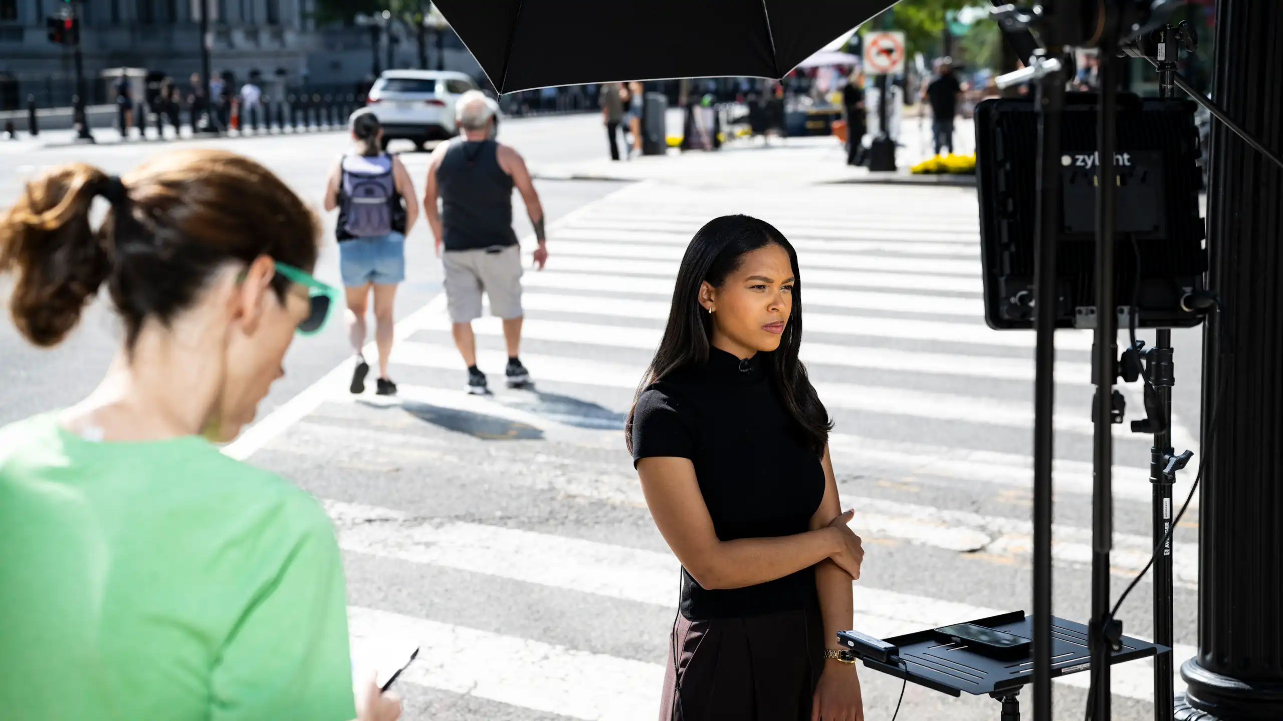 A woman in a black dress standing on a street corner, waiting for something.