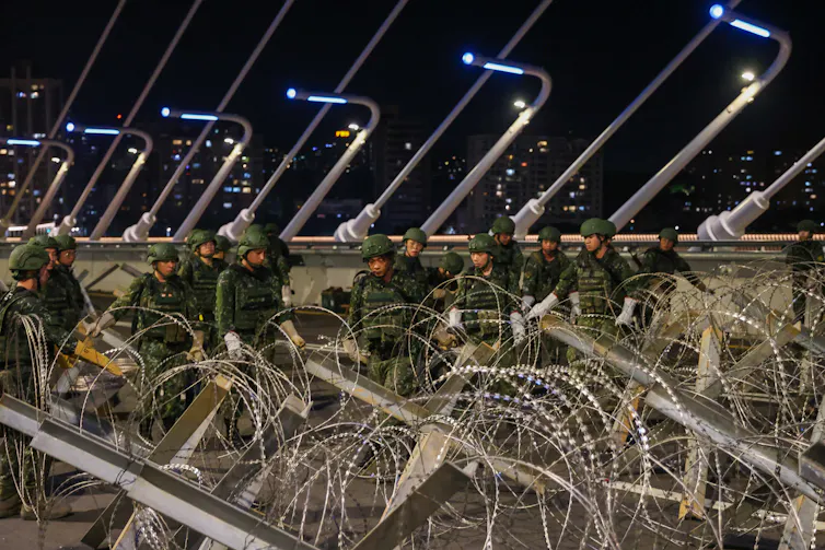 Men in army fatigues are seen behind barbed-wire.