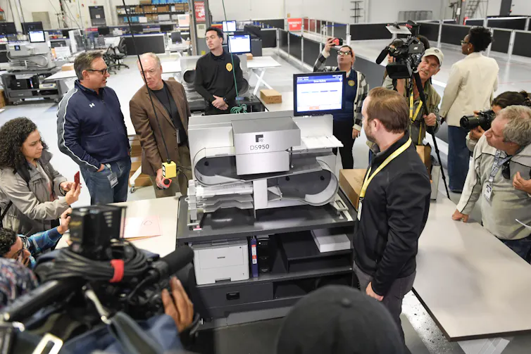 People in a large room standing around a machine.