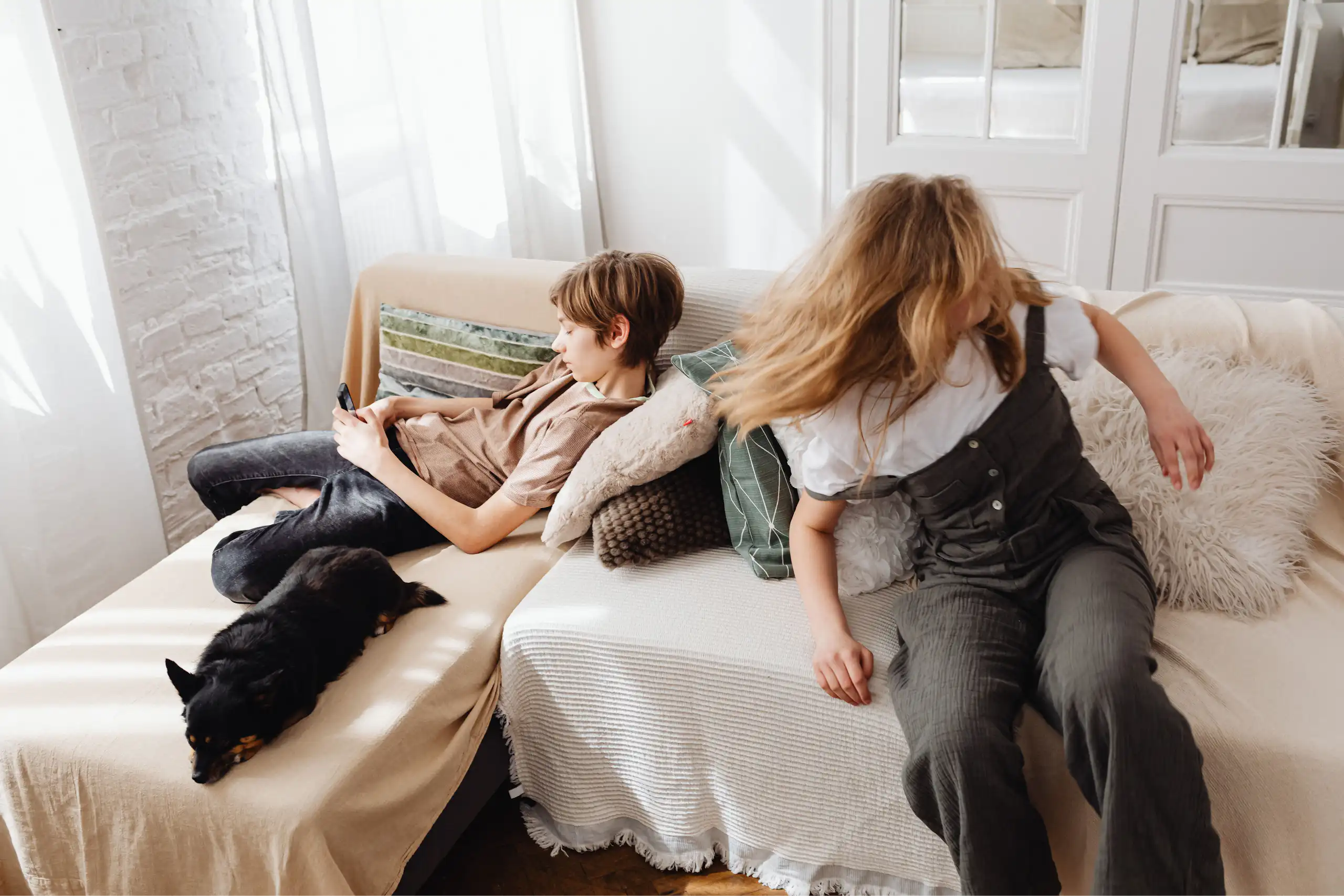 Two young people sitting on a couch. A boy is on a phone, a girl is turning her head quickly,