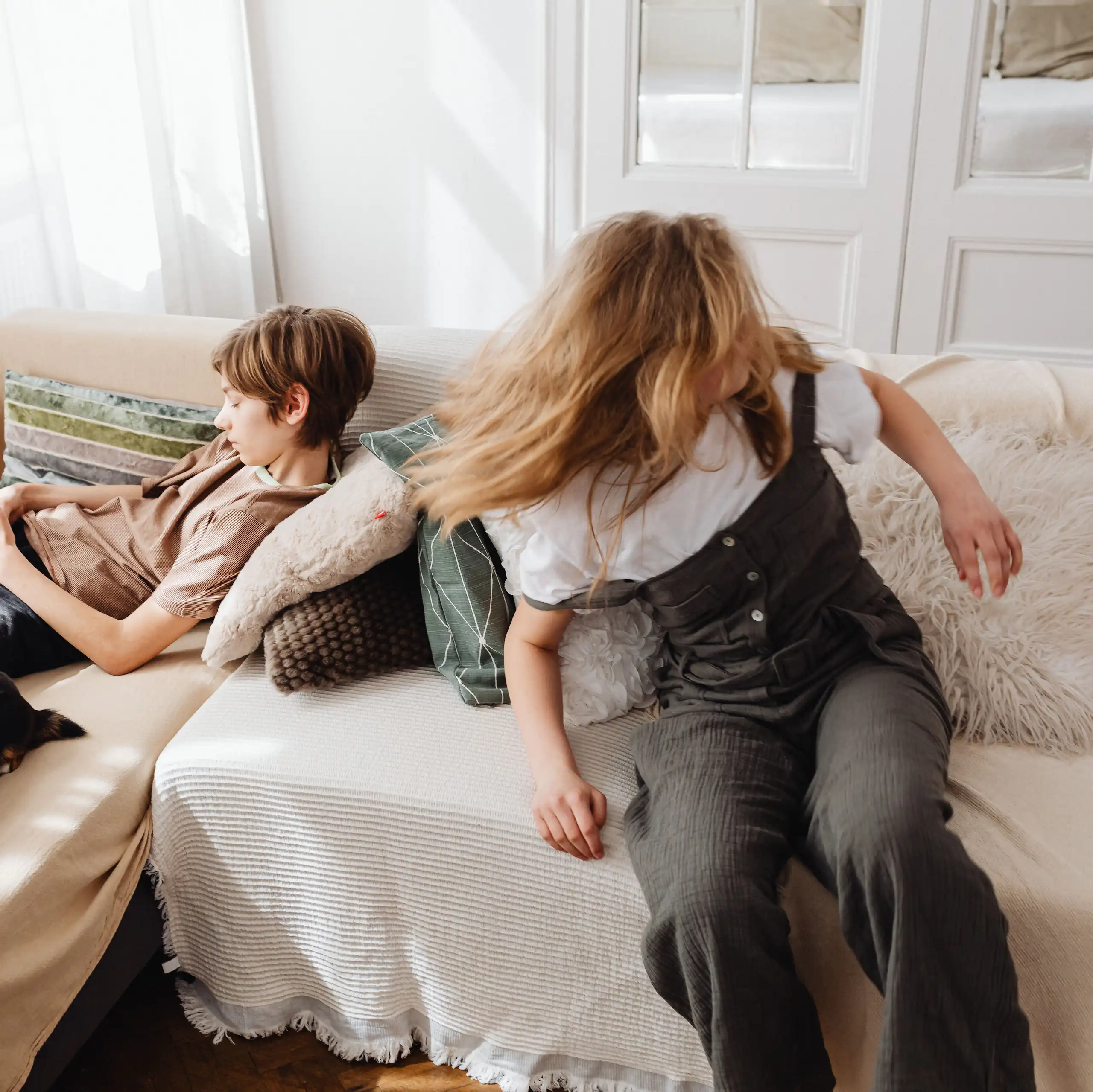 Two young people sitting on a couch. A boy is on a phone, a girl is turning her head quickly,