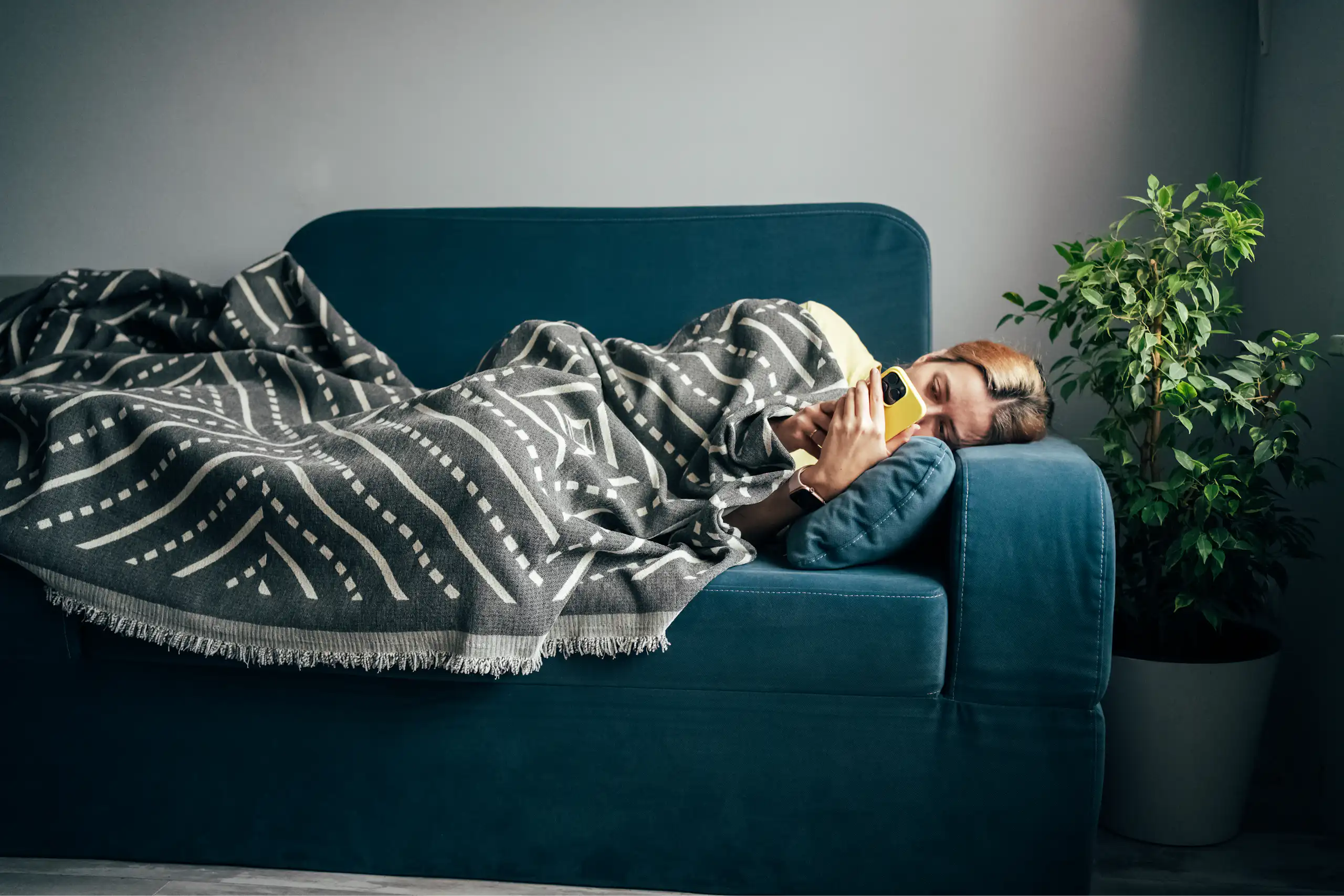 A woman with the flu lays on the couch, looking at her phone