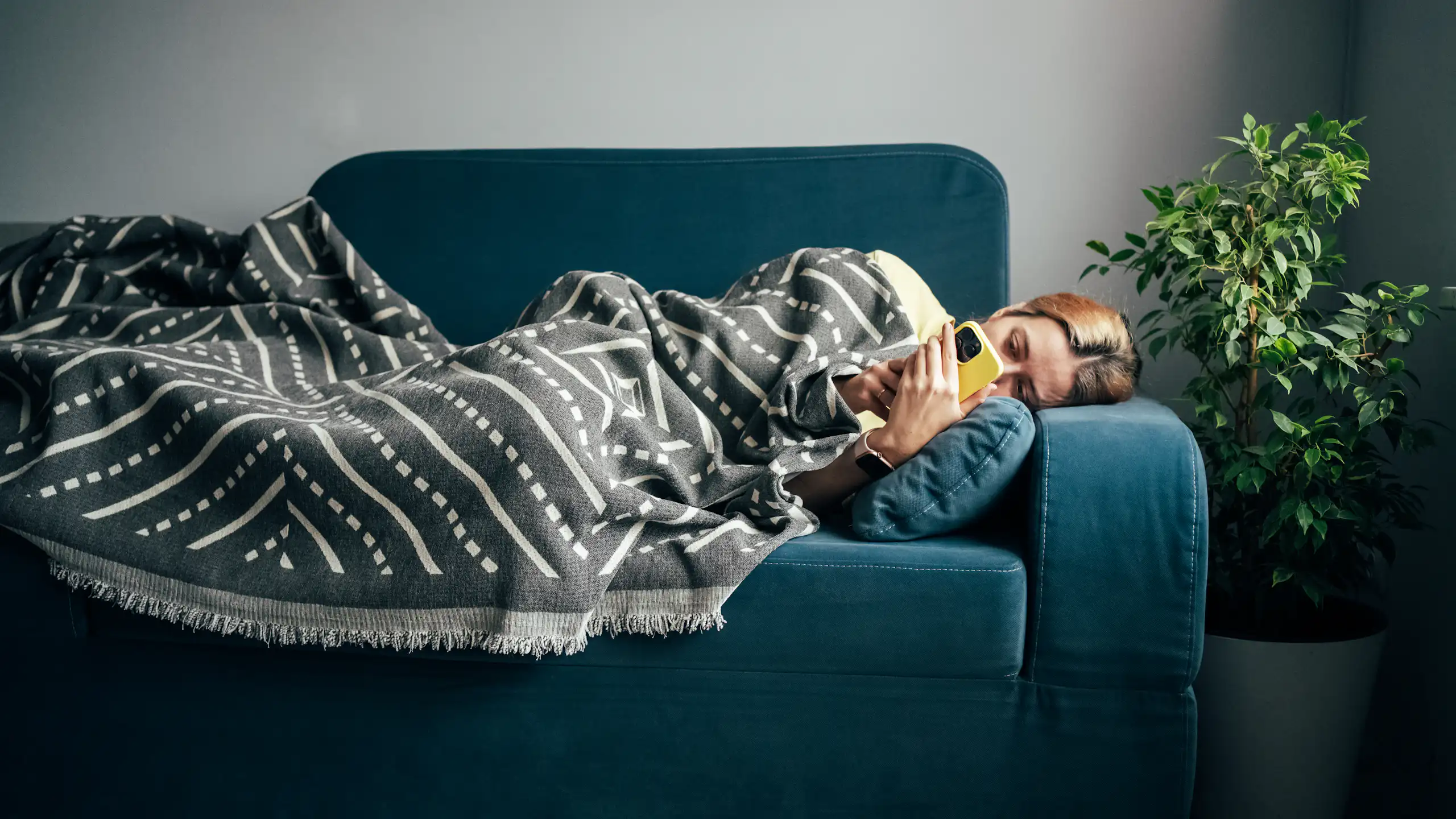 A woman with the flu lays on the couch, looking at her phone