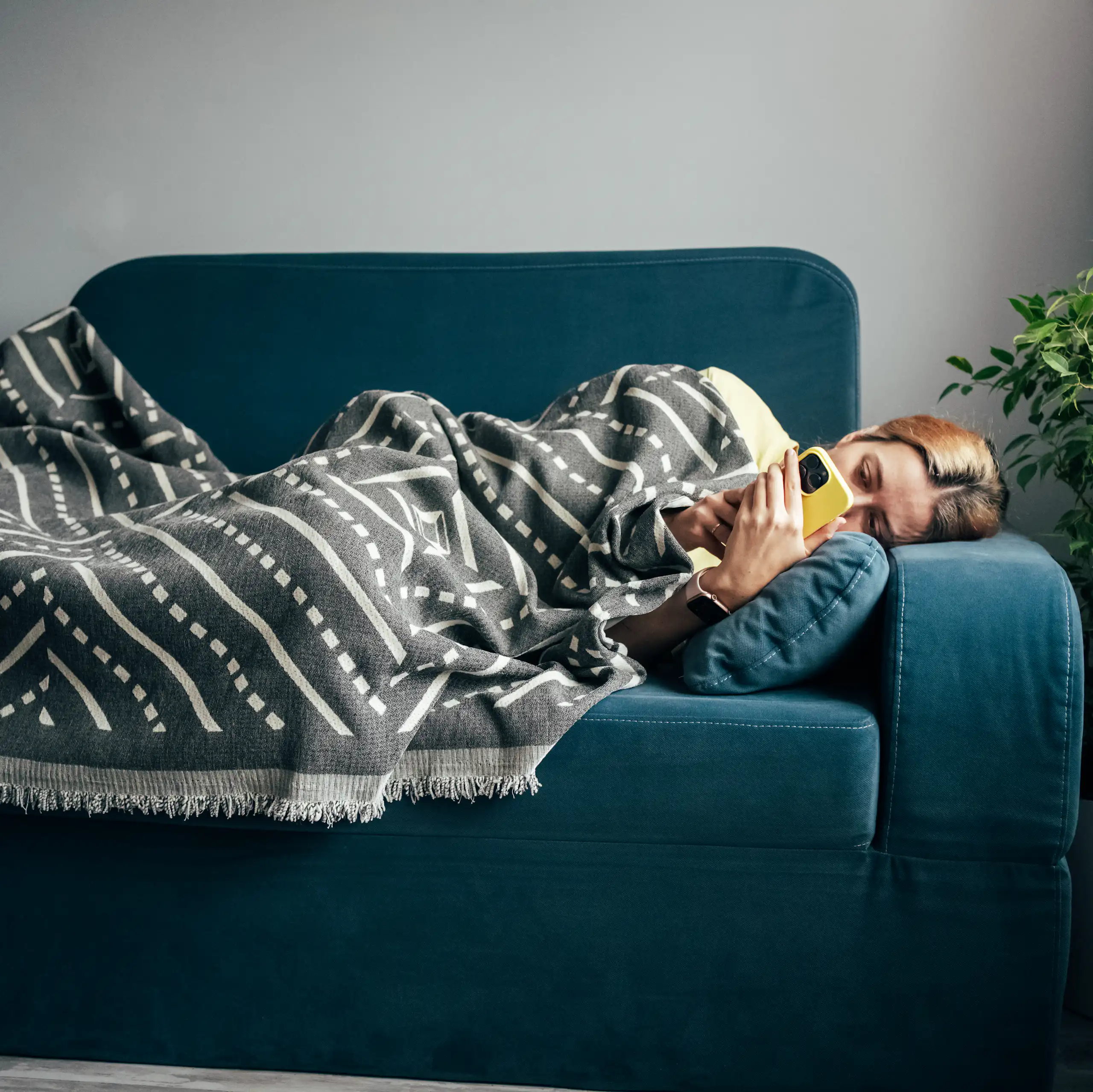 A woman with the flu lays on the couch, looking at her phone