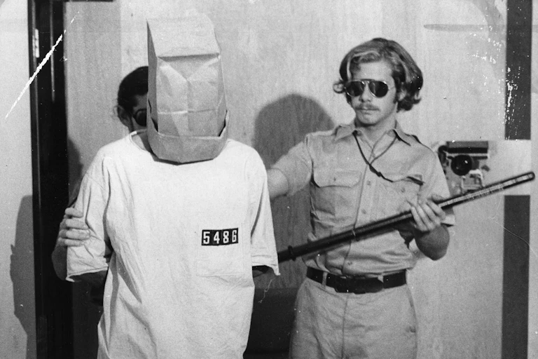 Photo of the experiment: Prisoner with paper bag over his head, with a guard.