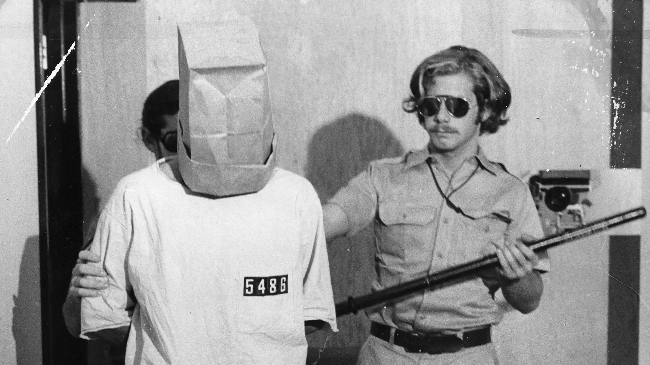 Photo of the experiment: Prisoner with paper bag over his head, with a guard.