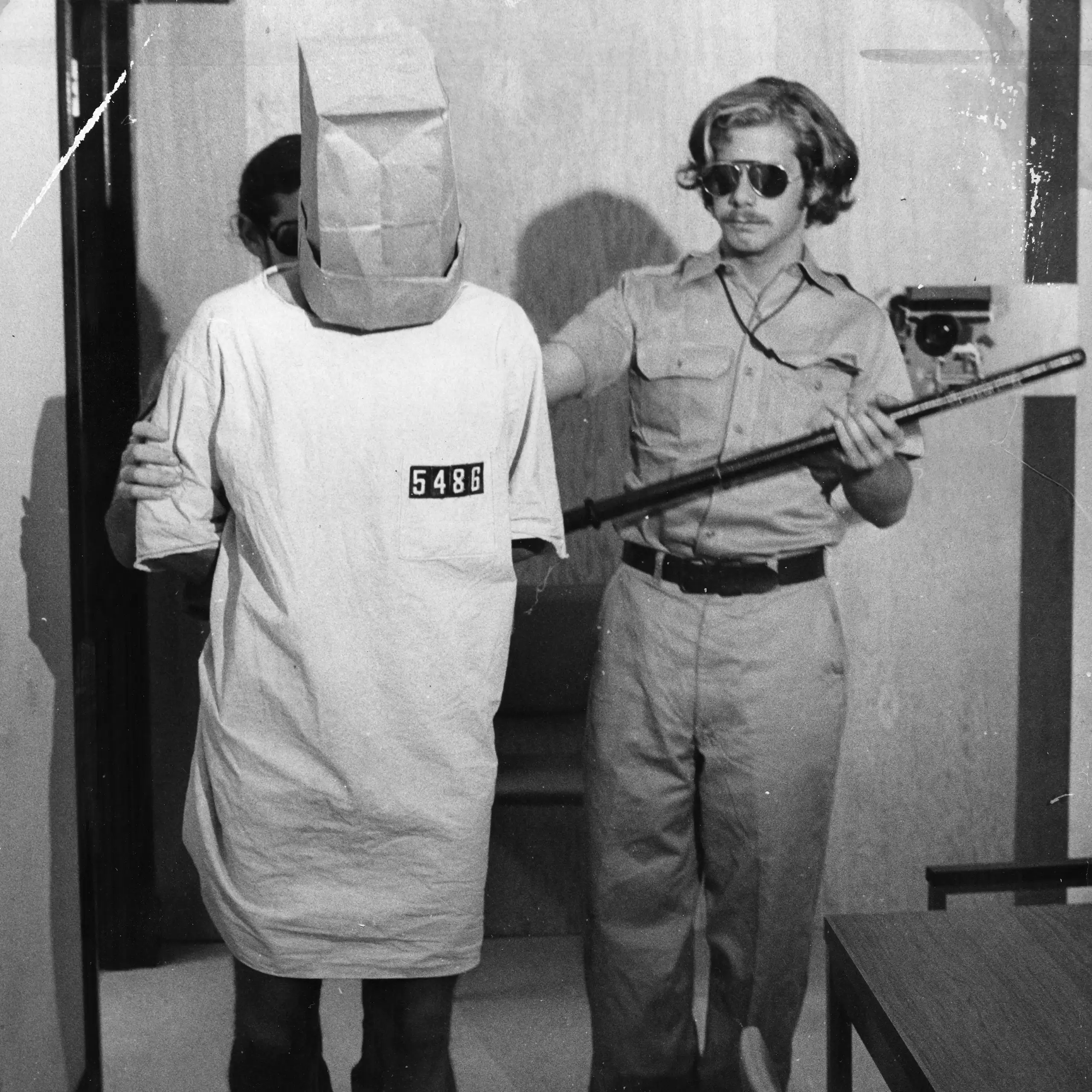 Photo of the experiment: Prisoner with paper bag over his head, with a guard.