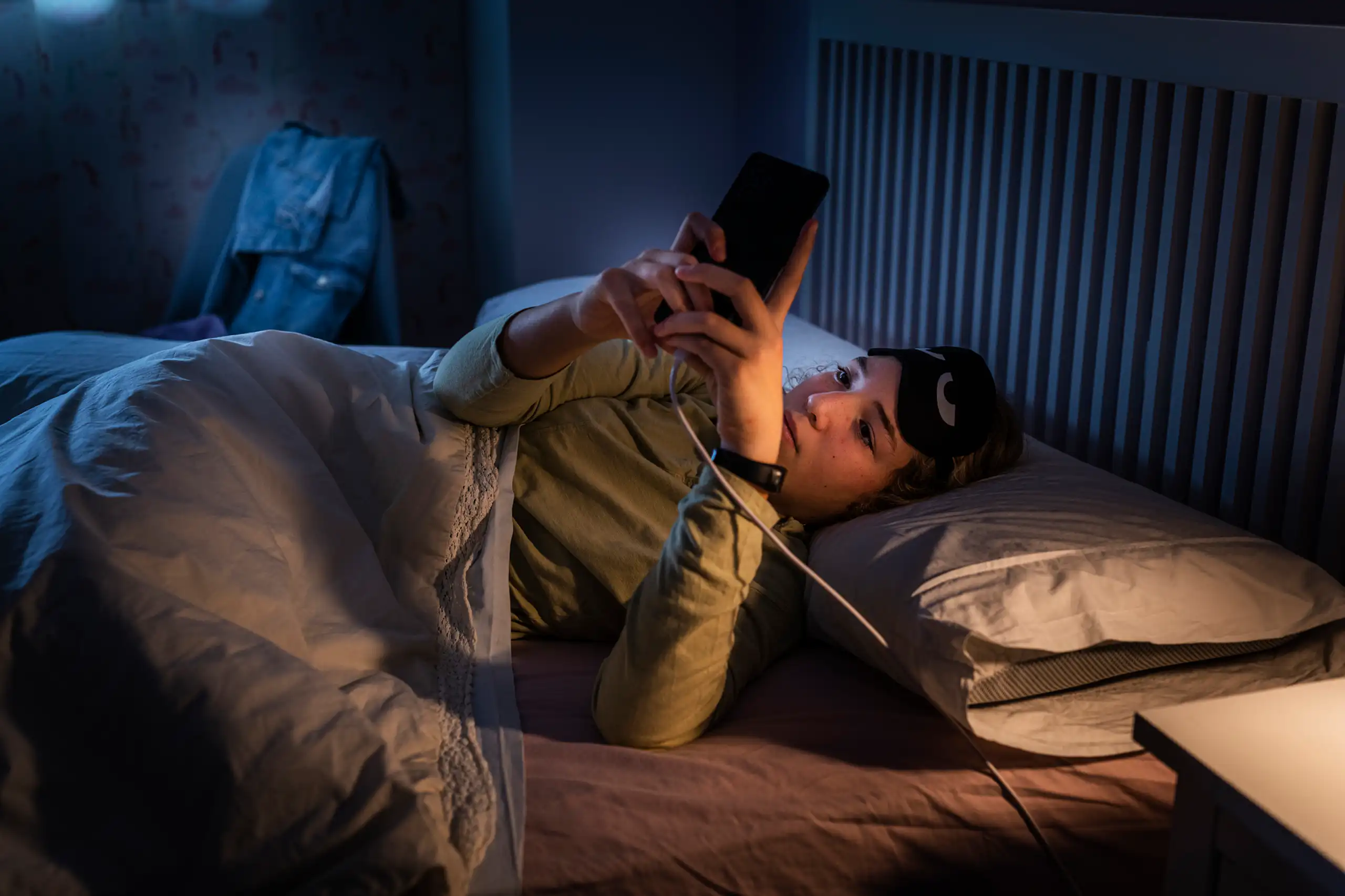 A woman at night looking at her phone that's plugged in by her bed.