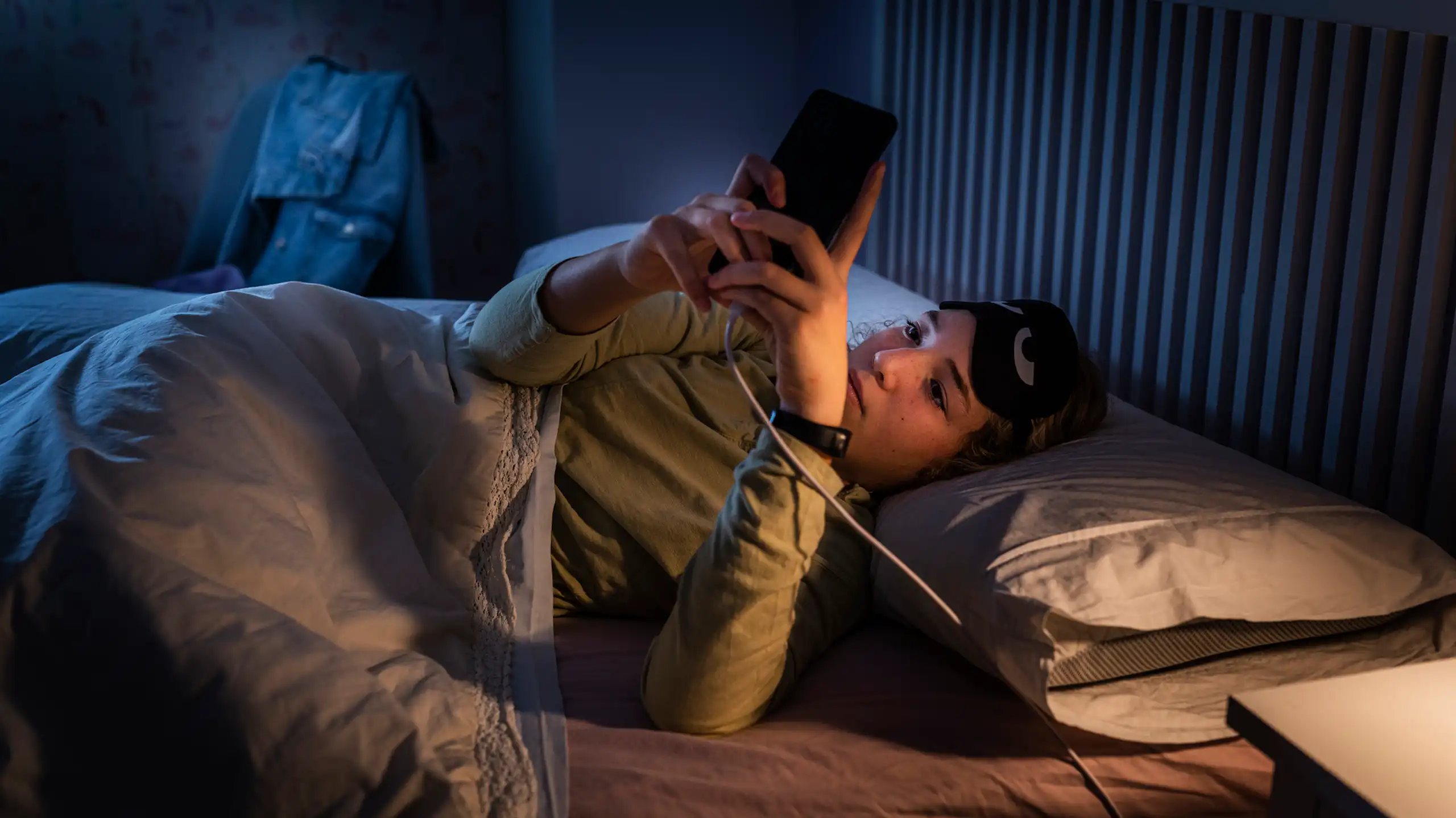 A woman at night looking at her phone that's plugged in by her bed.