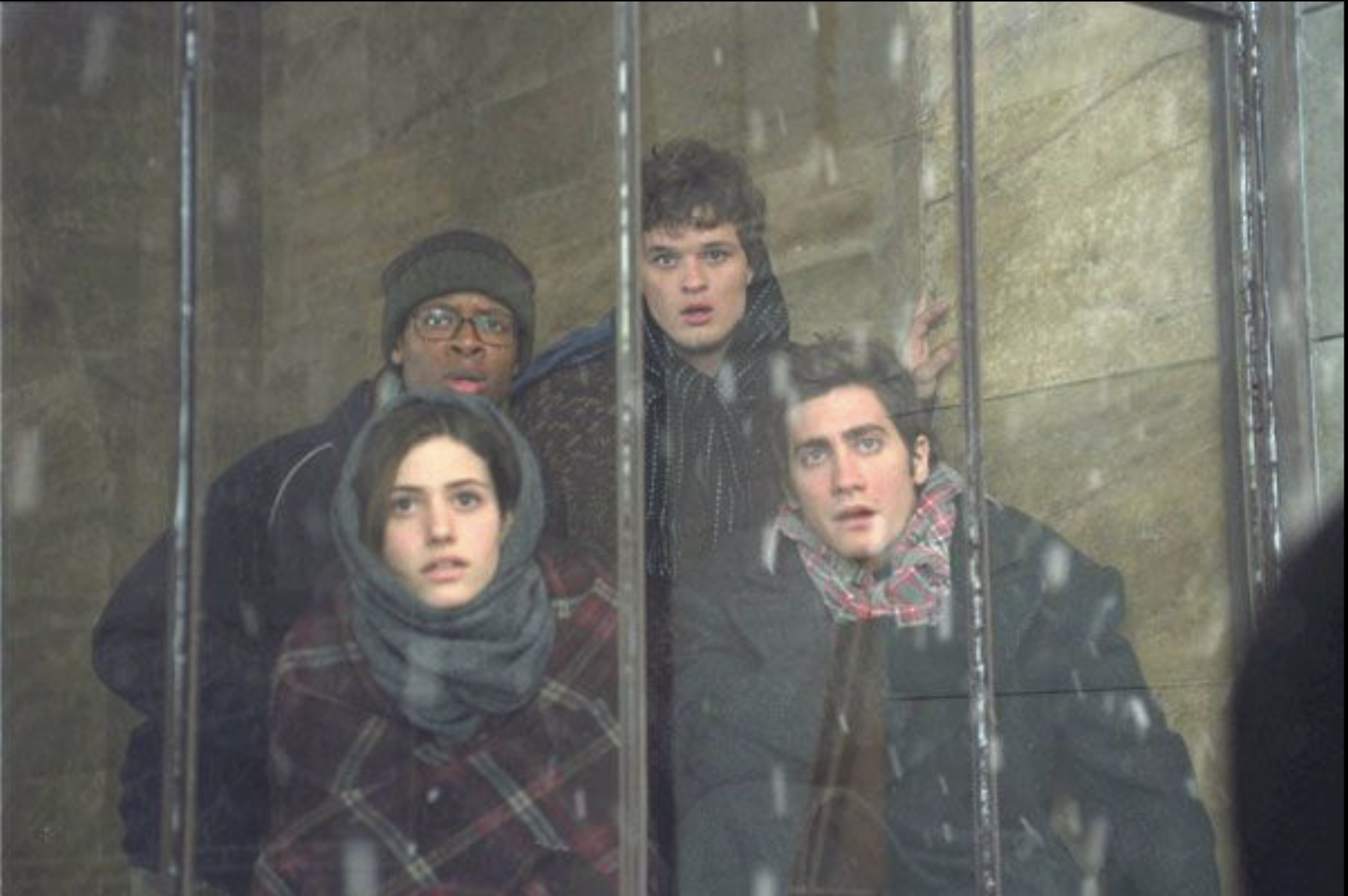 Quatre personnages du film regardent, tétanisés, à travers une baie vitrée.